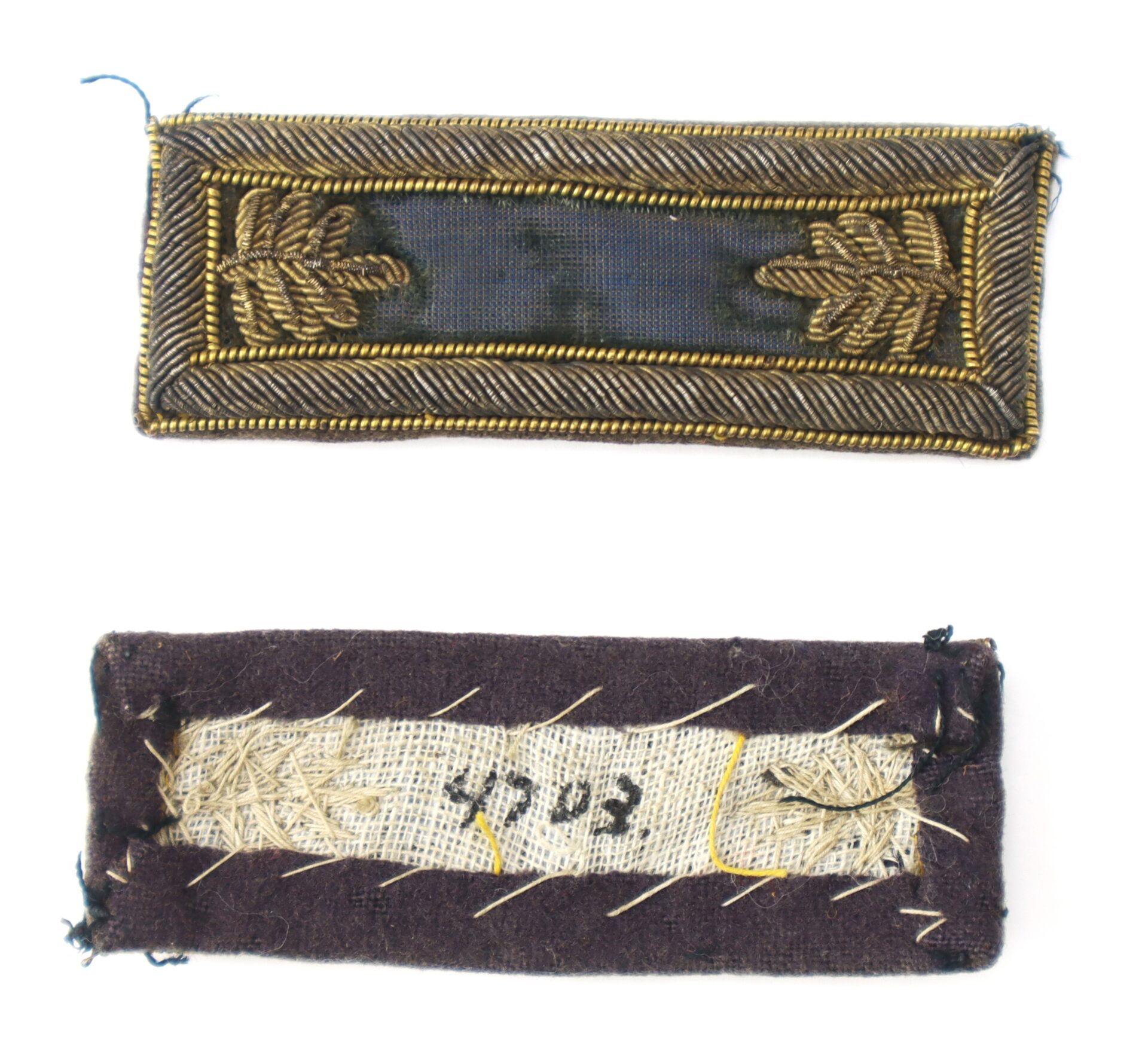 A rectangular embroidered patch with gold laurel leaf designs on a dark background, shown from the front and back. The back has visible stitching and handwritten numbers.