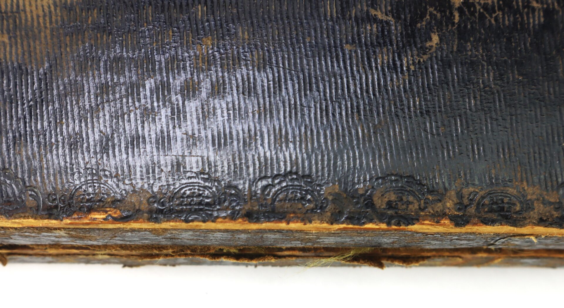 Close-up of a worn, black textured book spine with faded gold decorative embossing near the edge and visible signs of aging.