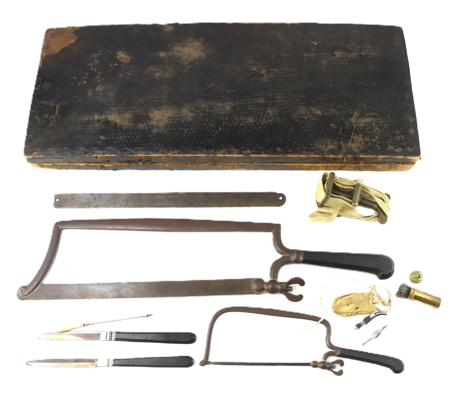 A vintage surgical amputation kit with saws, scalpels, tourniquet, bone key, and a black storage box laid out on a white background.