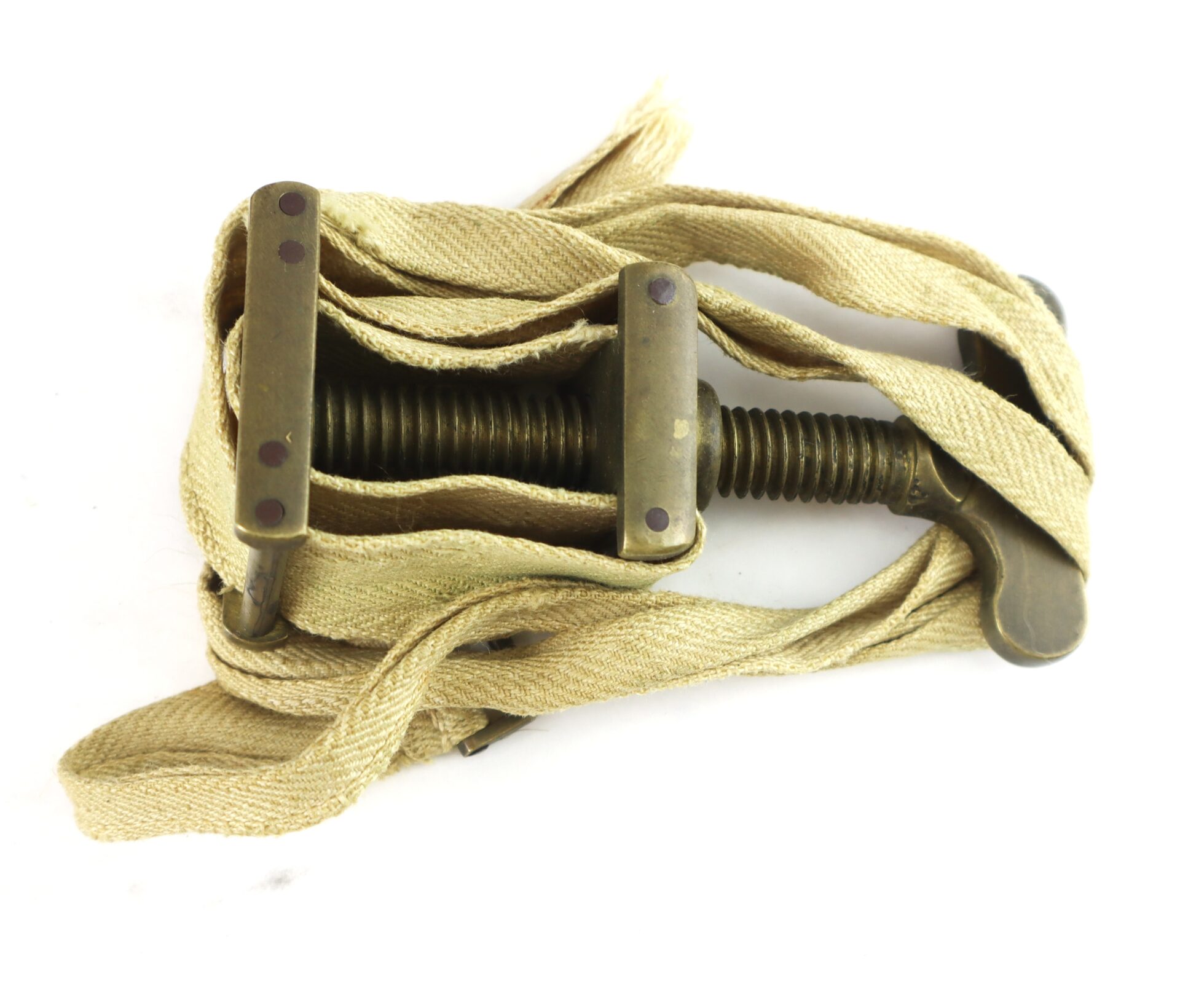 A vintage metal tourniquet with a screw mechanism and attached fabric strap, coiled loosely around the device.