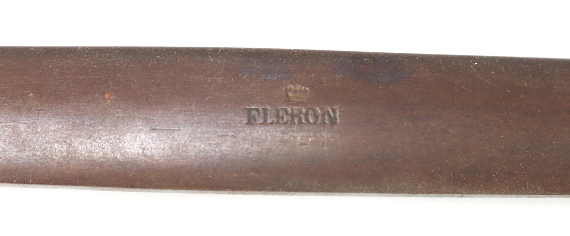 Close-up view of a brown metal object with the word "ELBRON" and a small crown symbol stamped on its surface.