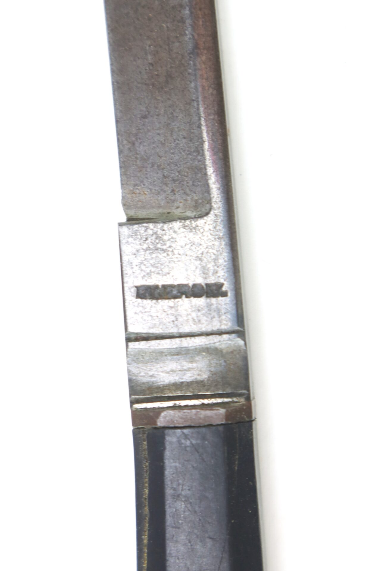 Close-up of a metal object with the word "IMPROVED" engraved on it, showing part of a blade and handle against a white background.