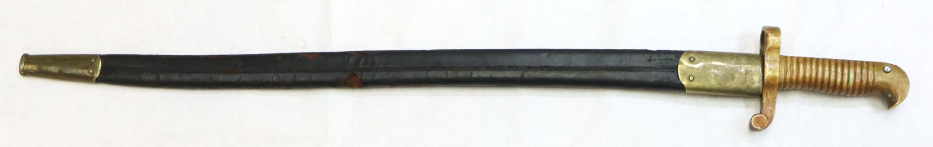 A short sword or bayonet with a brass hilt and curved guard, sheathed in a black scabbard with brass fittings, displayed on a white background.