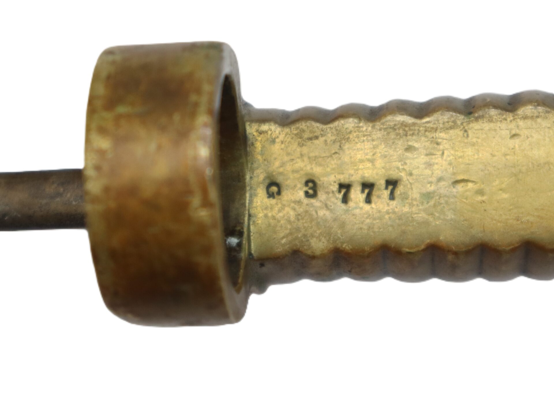 Close-up of a brass object with a ridged handle and the marking "G 3777" stamped on its surface.