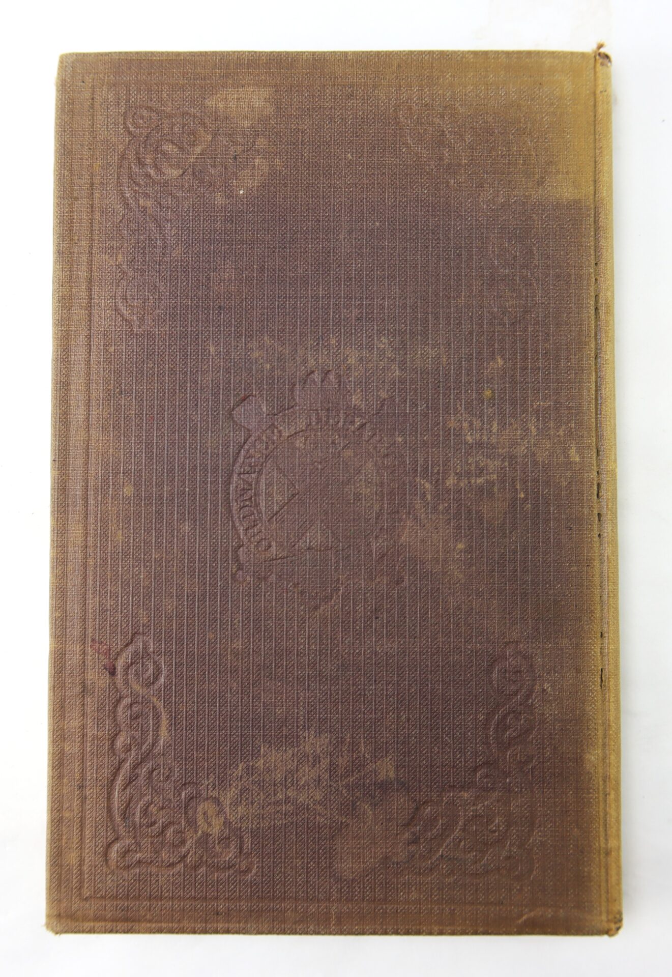 A worn, brown hardcover copy of the 1863 Ordnance Bureau Manual, identified to William A. Barker of the 4th Maine Volunteer Infantry, with embossed patterns and cover discoloration, rests on a white surface.