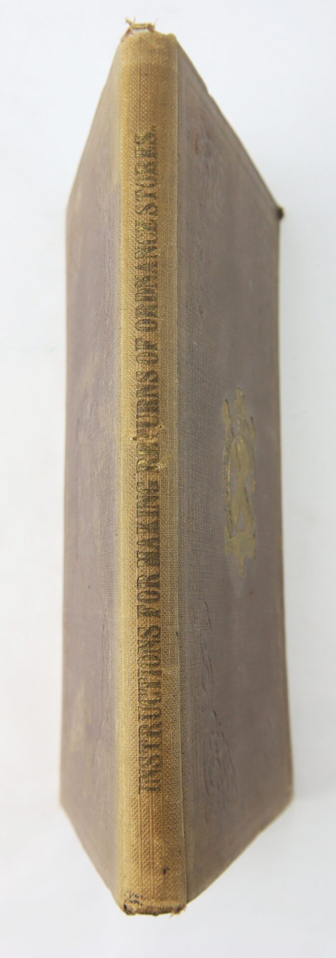 An aged brown hardcover, spine view, shows faded gold text and a decorative emblem; it’s the 1863 Ordnance Bureau Manual identified to William A. Barker of the 4th Maine Volunteer Infantry.