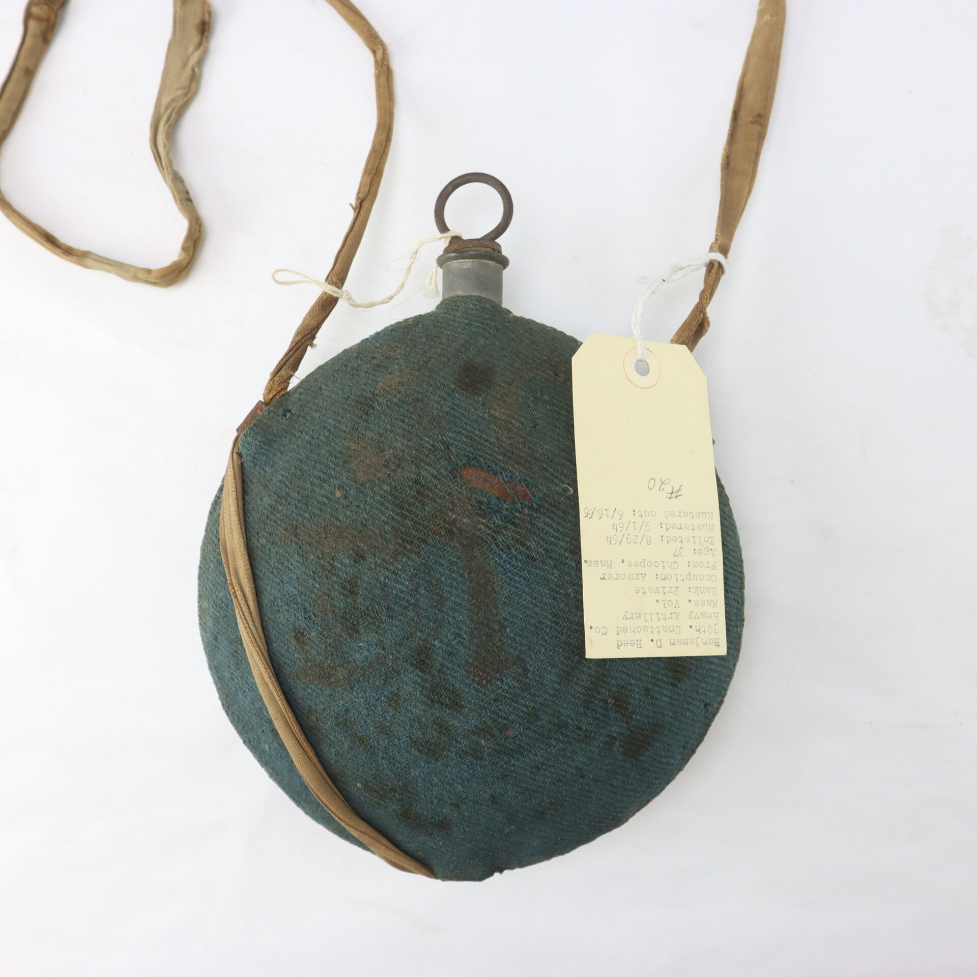 Outstanding Identified Massachusetts Heavy Artillery Canteen: Round, green fabric-covered canteen with a long strap, metal cap, and paper tag, once carried by Benjamin D. Reed of the 30th Unattached Co., Mass. Heavy Artillery, shown on a white background.