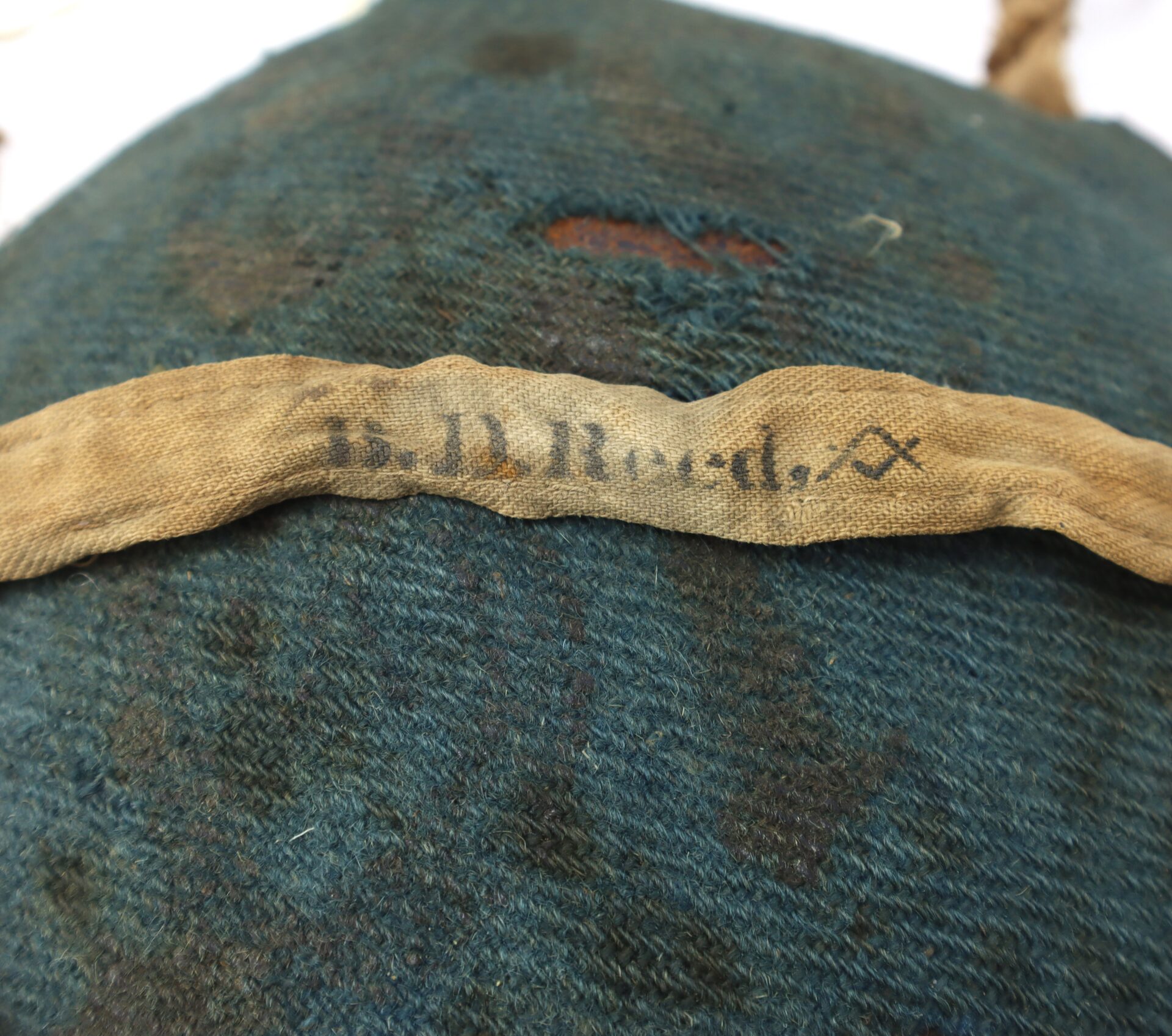 A close-up of a worn fabric label reading “B. D. Reed,” sewn onto the dark, frayed cloth of an Outstanding Identified Massachusetts Heavy Artillery Canteen from Benjamin D. Reed, 30th Unattached Co., Mass. Heavy Artillery.