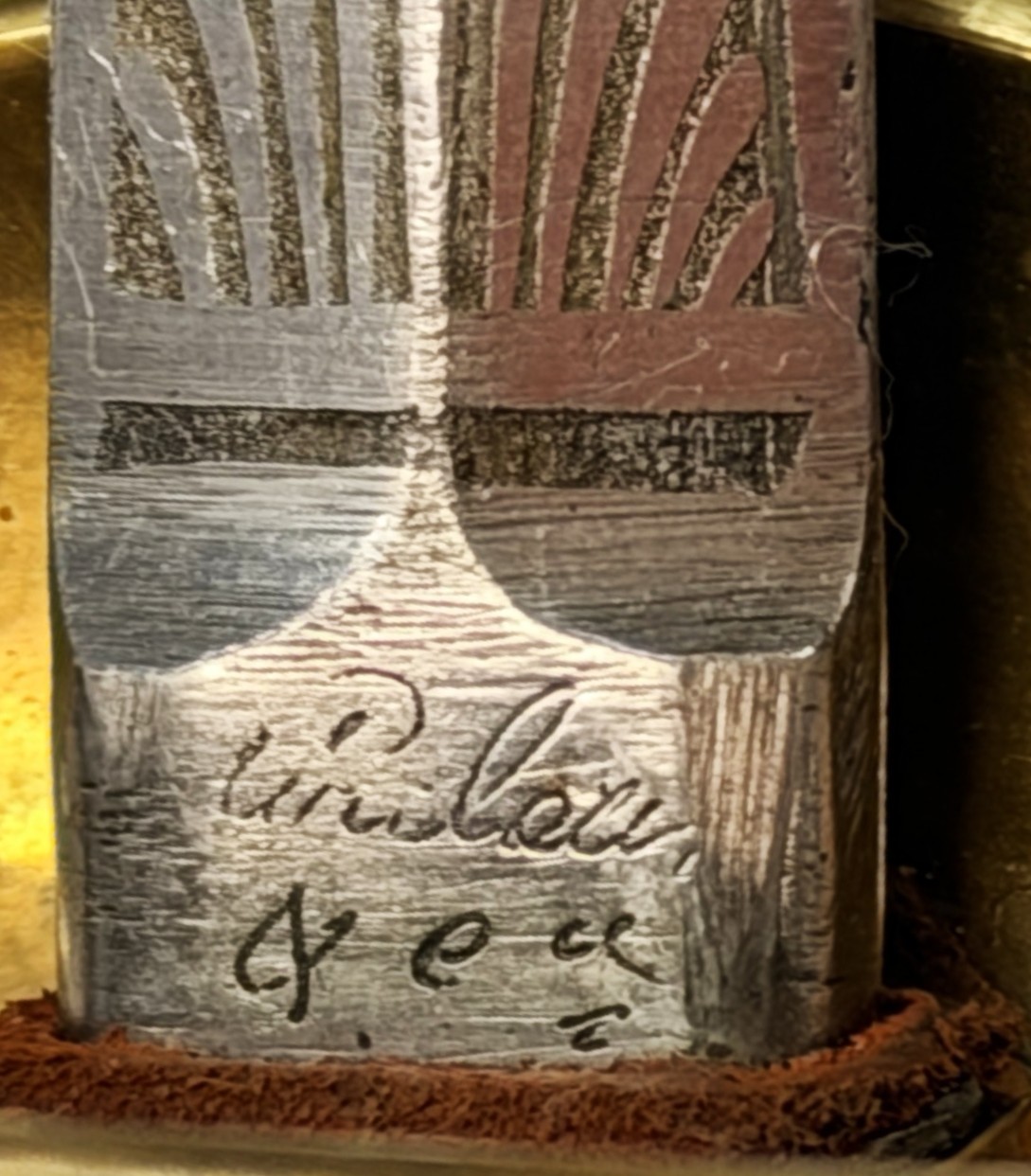 Close-up of a metal fountain pen nib with engraved patterns and cursive signature, shown against a blurred background.
