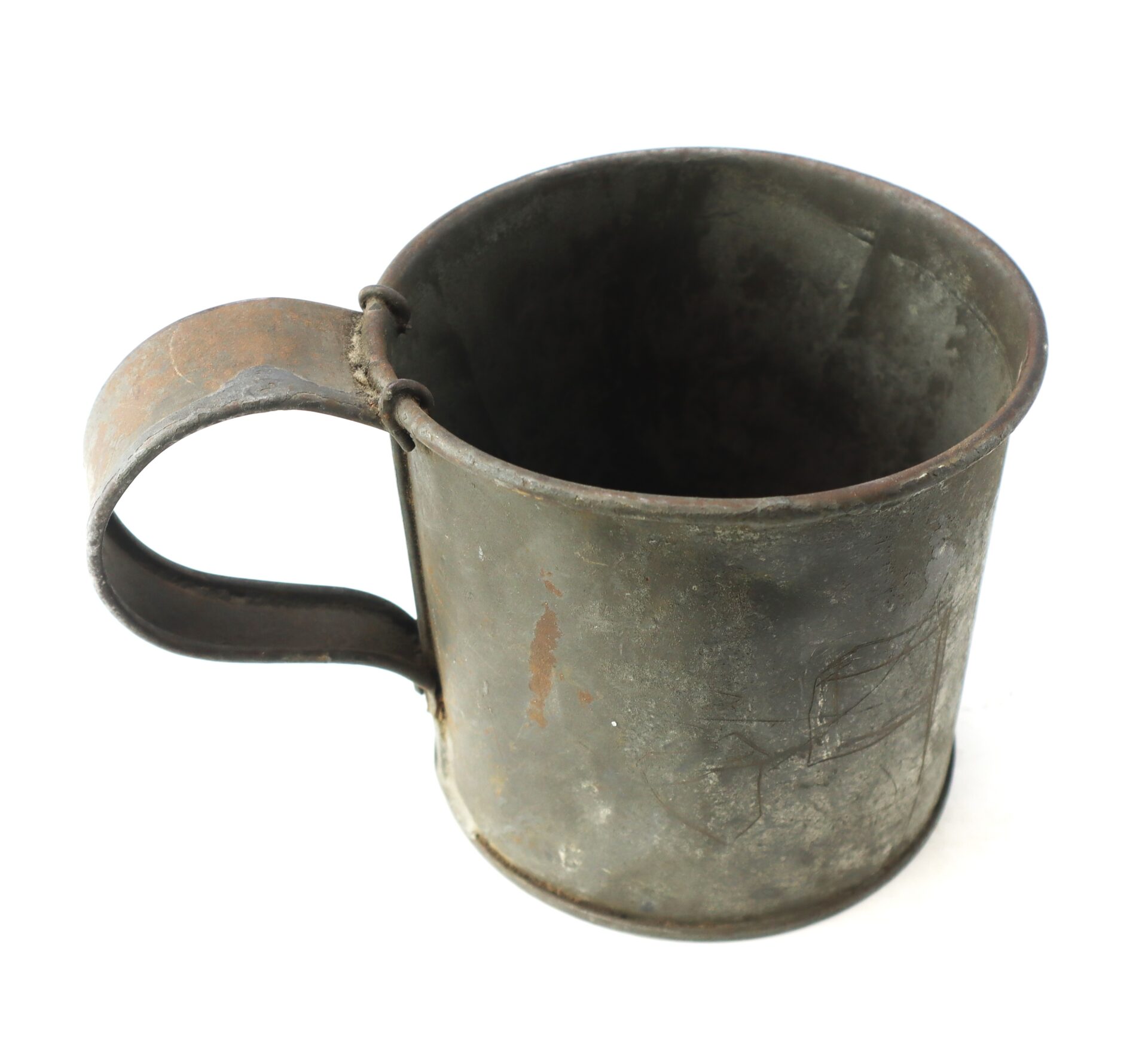An old, worn metal mug with a large handle, showing signs of rust and discoloration, photographed on a white background.
