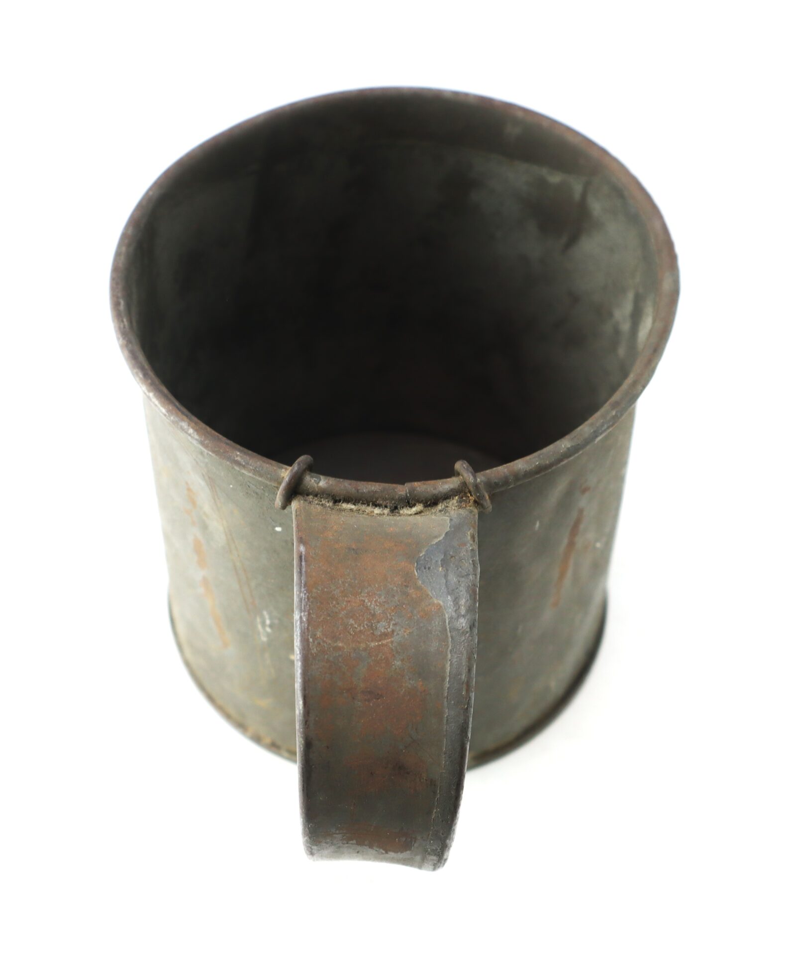 A weathered, empty metal cup with a handle, shown from above against a white background.