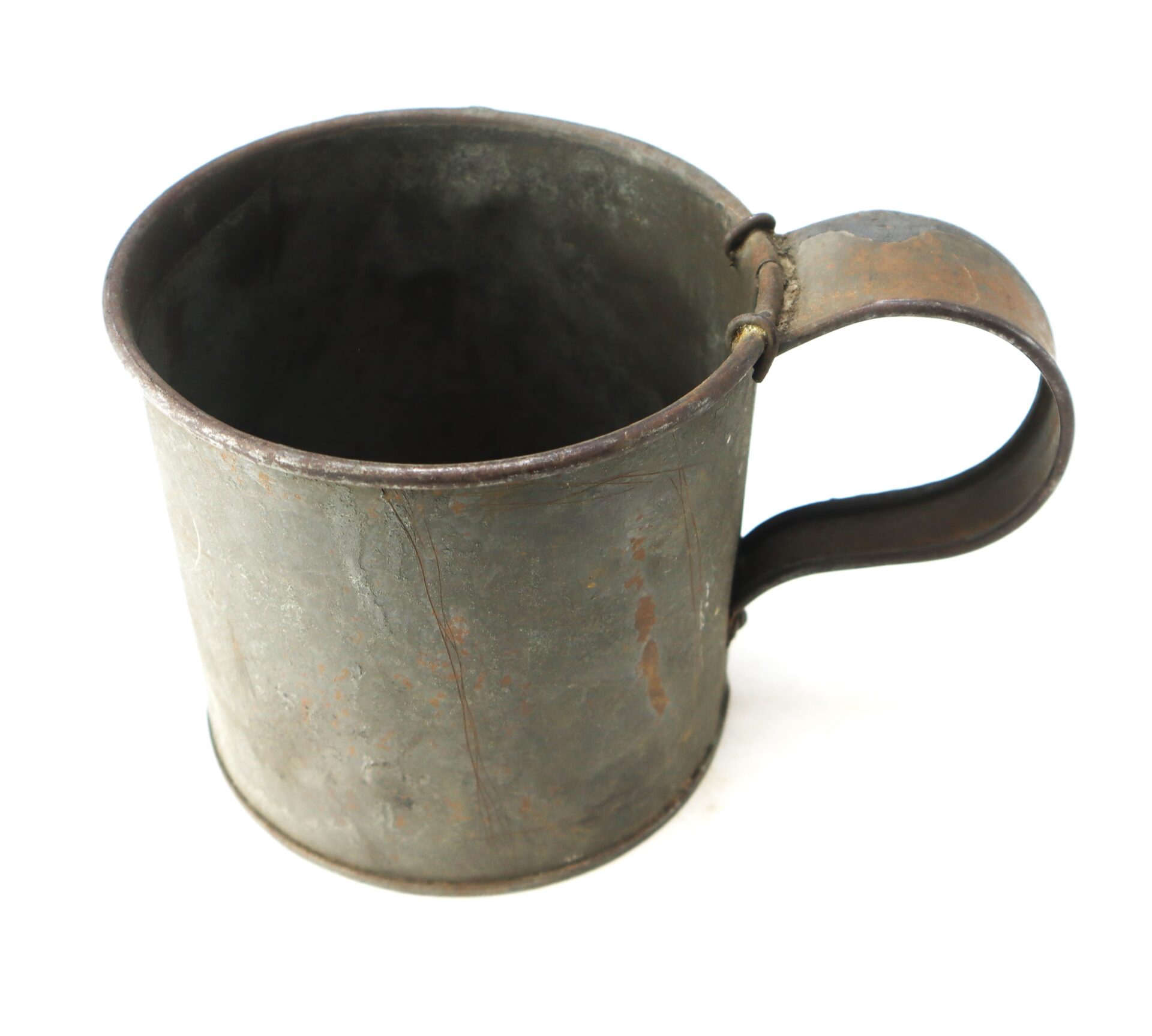 A weathered, metal mug with a large handle, showing visible rust and signs of age, photographed on a white background.