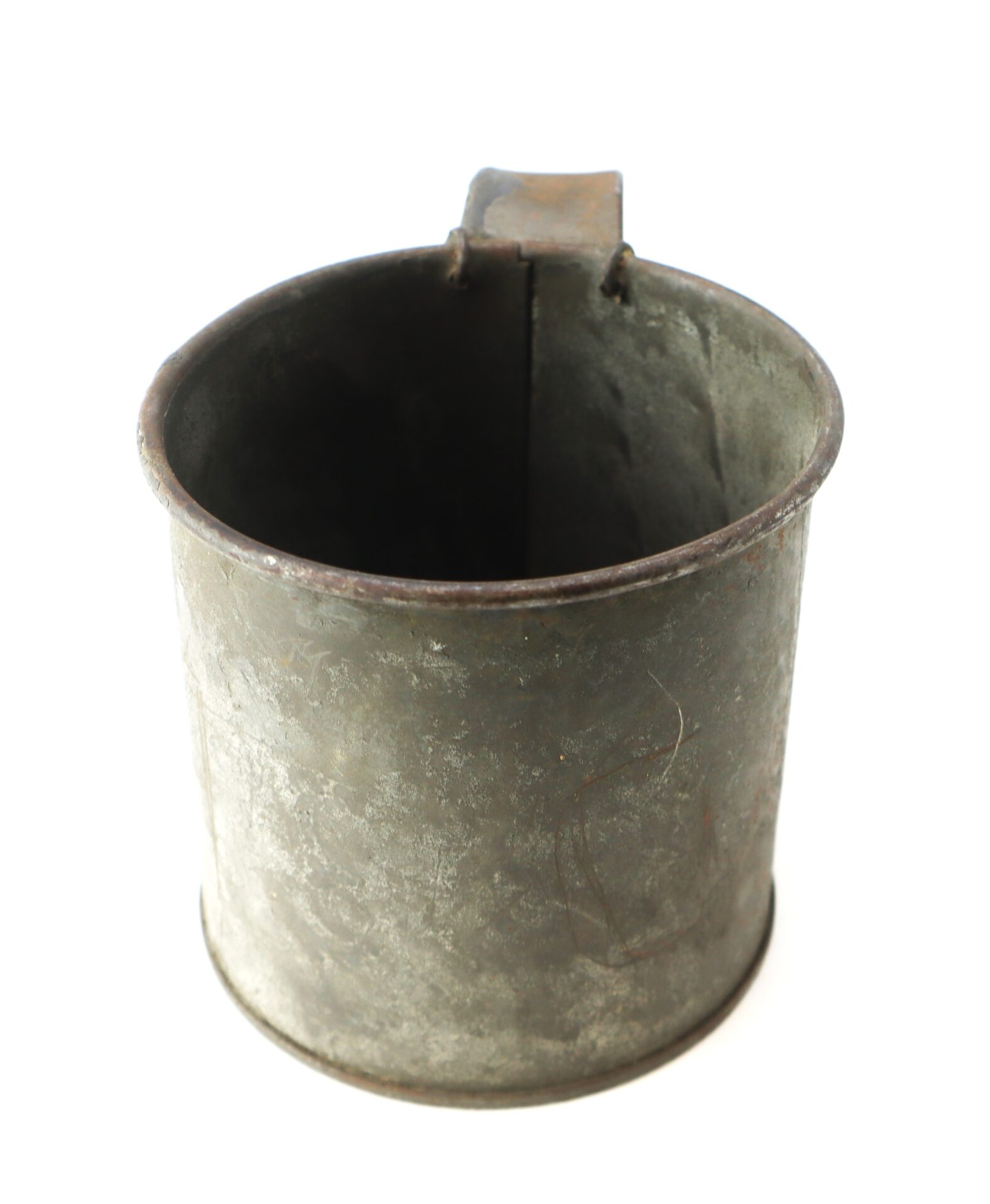 A metal cup with a handle, showing signs of wear and oxidation, photographed on a white background.