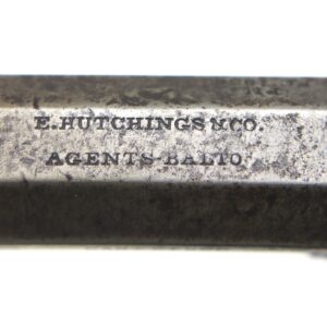 Close-up of a metal object engraved with the words "E. Hutchings & Co. Agents Bath". The surface appears worn and aged.