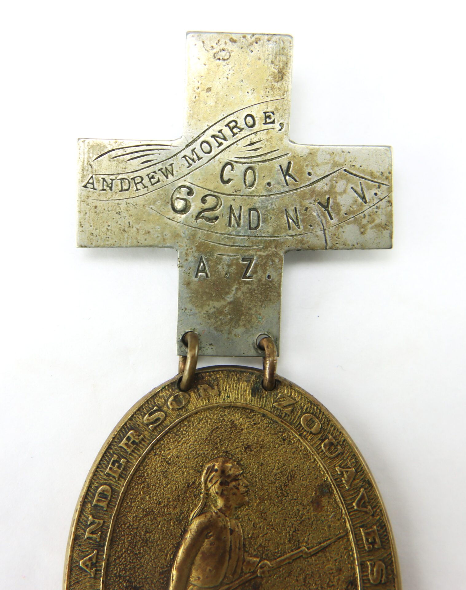 A metal cross-shaped medal engraved with "Andrew Monroe, Co. K, 62nd N.Y.V." is attached to an oval medallion featuring a raised image of a soldier holding a rifle.