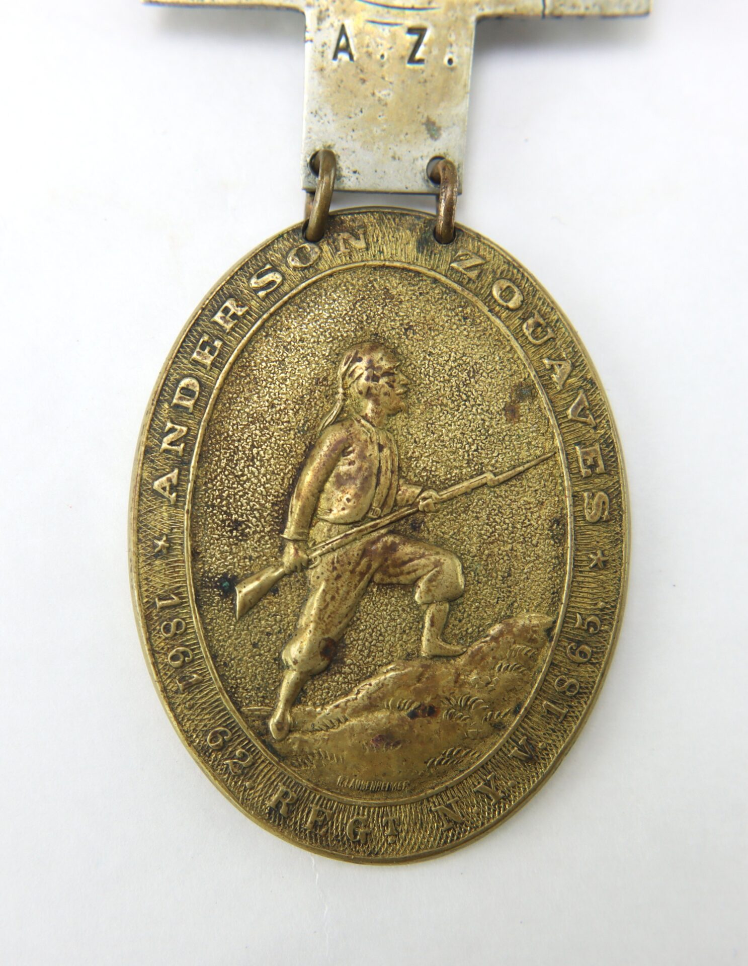 Oval-shaped brass medal with a raised image of a soldier holding a rifle; text reads "ANDERSON ZOUAVES 1861-1865" around the edge.