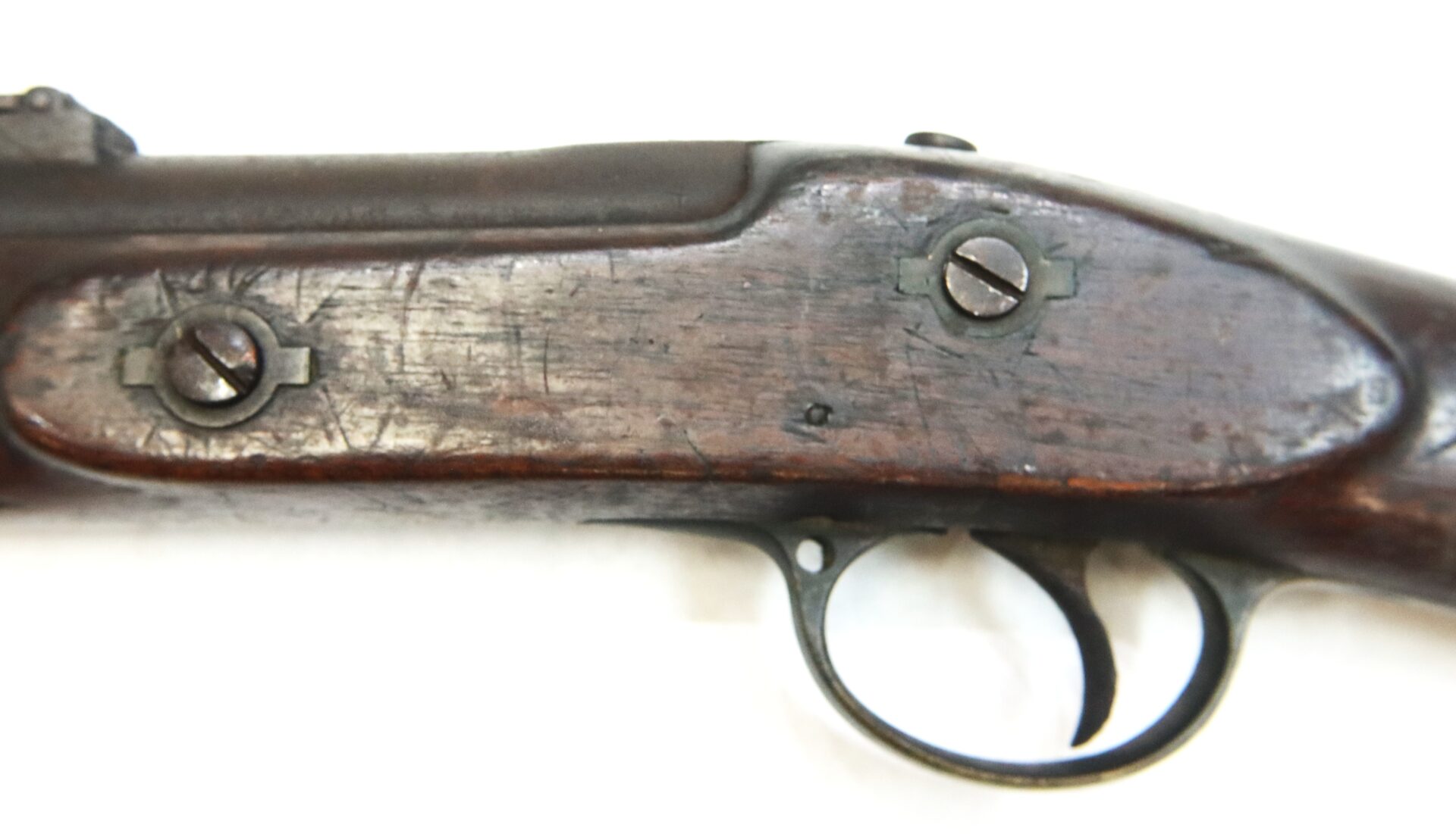 Close-up view of the trigger and side plate area of an old, worn wooden rifle stock with visible screws and scratches.