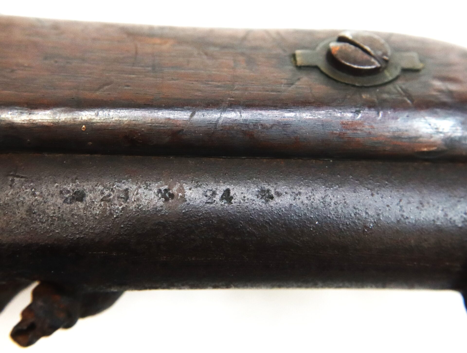 Close-up of a worn, dark wooden and metal surface of an old firearm, showing a screw and faint markings on the metal barrel.