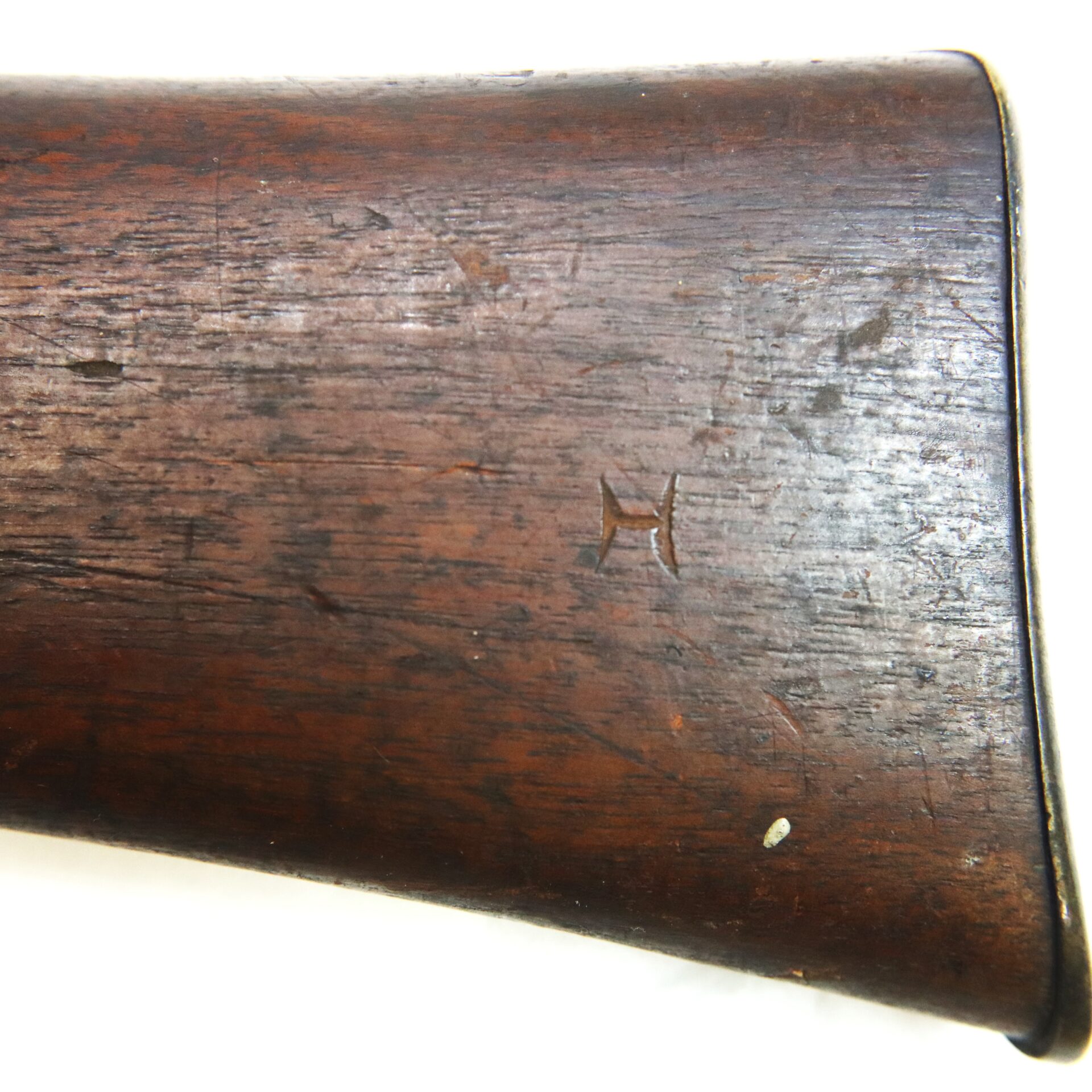 Close-up of a wooden gun stock with a carved 'H' mark and visible scratches and wear.