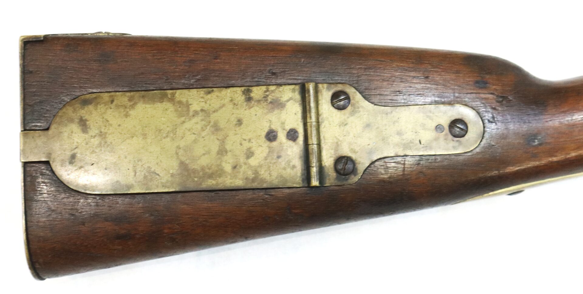 Close-up of a rifle's wooden stock with a brass patch box cover attached to the side.