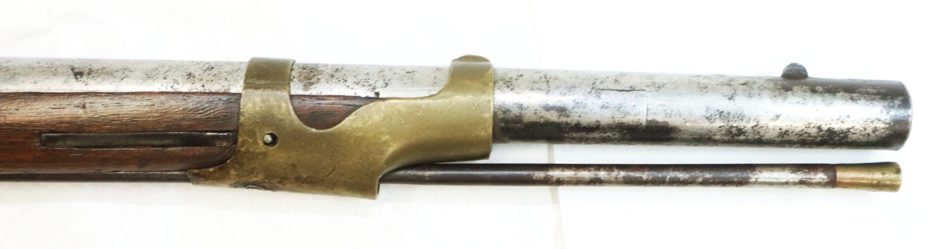 Close-up of the barrel and ramrod of an antique rifle with a brass barrel band and wooden stock, shown on a white background.