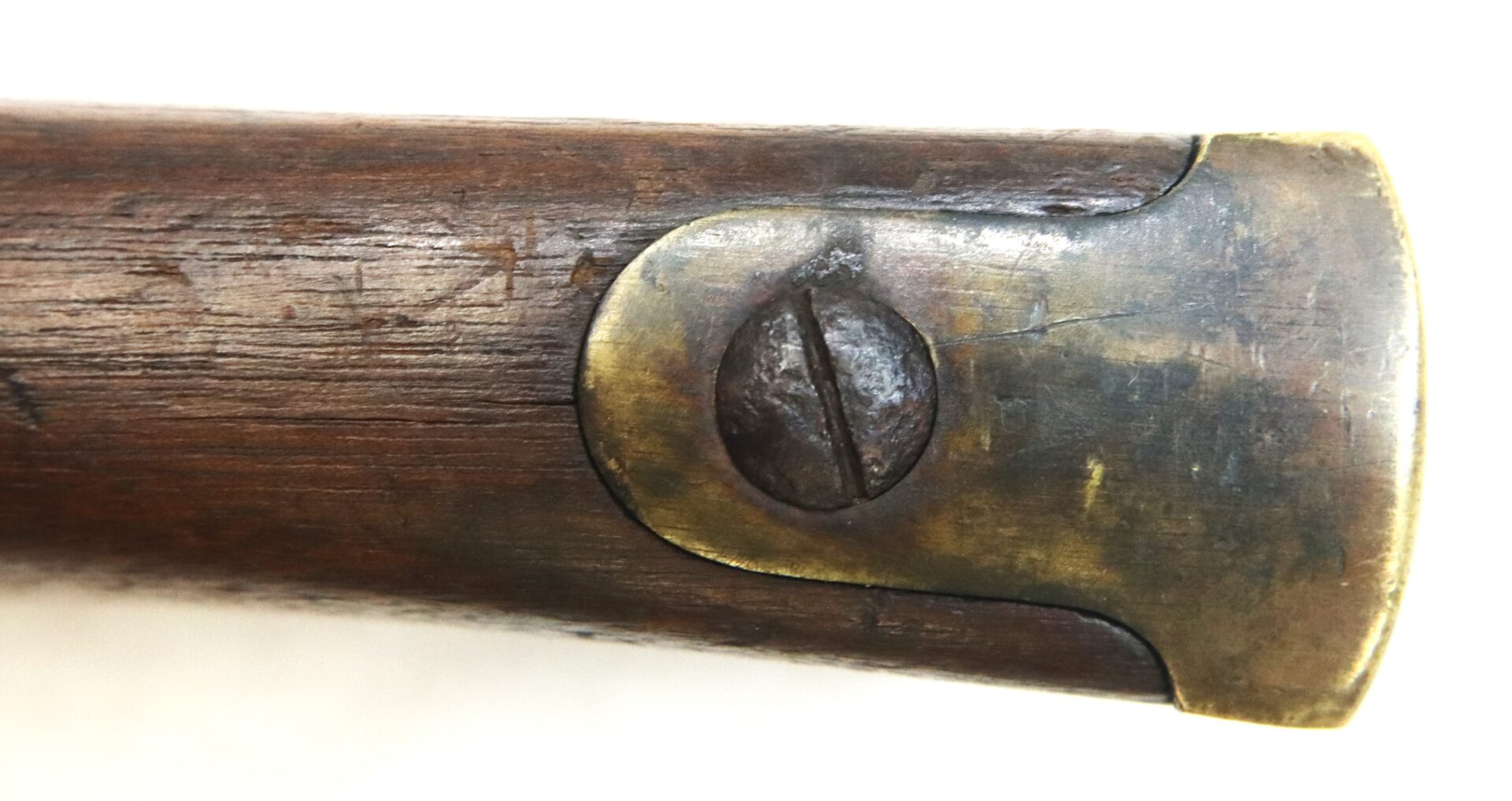 Close-up of a brass buttplate with a flathead screw on the wooden stock of a firearm.