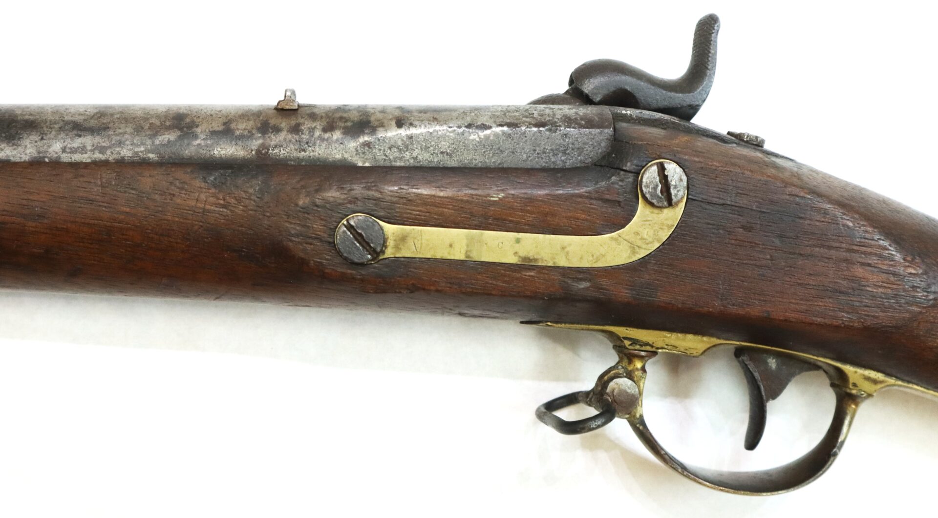 Close-up of an antique flintlock or percussion rifle showing a wooden stock, metal barrel, brass trigger guard, and hammer mechanism.