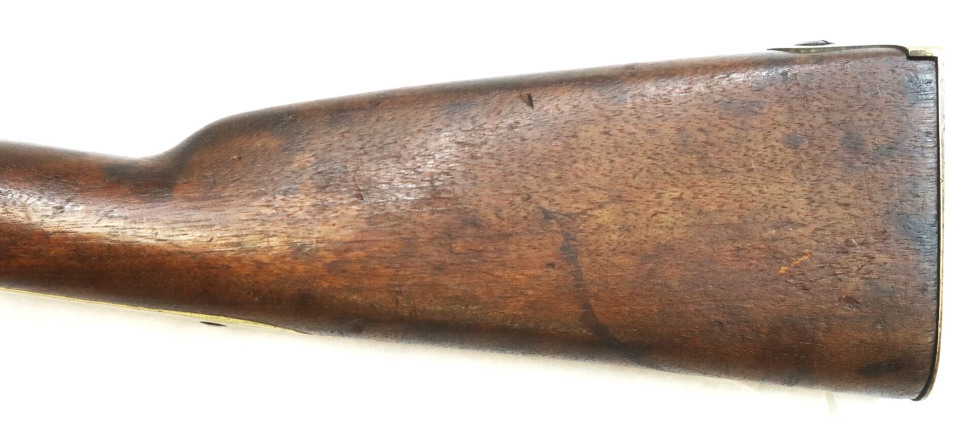 Close-up view of the wooden stock of a rifle, showing a worn and aged surface with some scratches and marks.