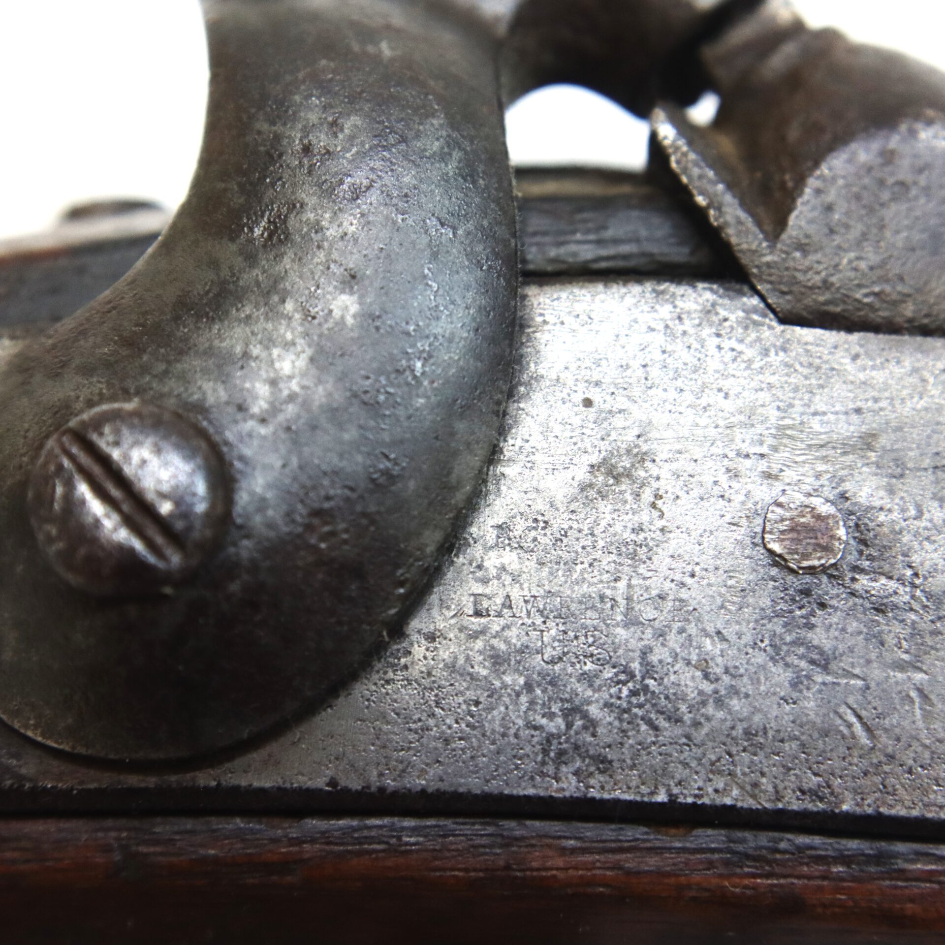 Close-up of an old, weathered metal firearm mechanism showing screws, textured surfaces, and signs of rust and wear.