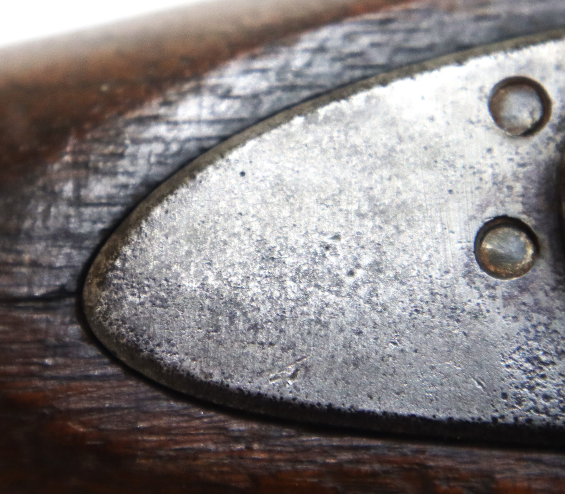 Close-up of a weathered metal plate with two screws attached to a piece of worn, dark wood.