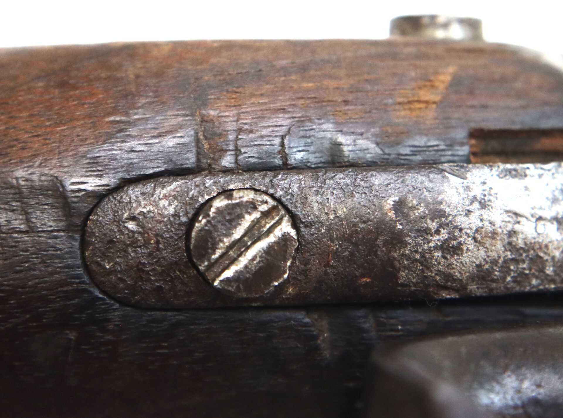 Close-up of a worn, rusted metal screw on a piece of aged, scratched wood, possibly part of an old firearm or tool.