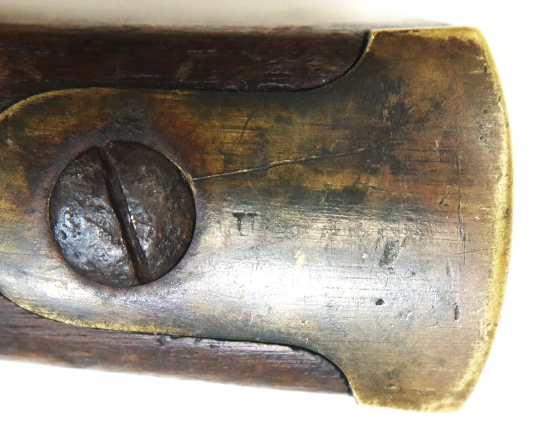 Close-up of a worn brass buttplate with a flathead screw on a wooden rifle or shotgun stock, showing signs of age and use.