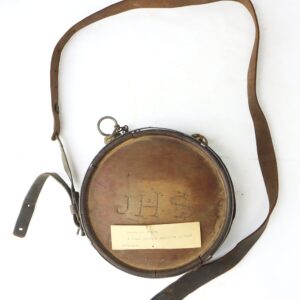 Round wooden canteen with leather strap, metal rim, and the initials "JHS" carved on the front; features an old paper label attached.