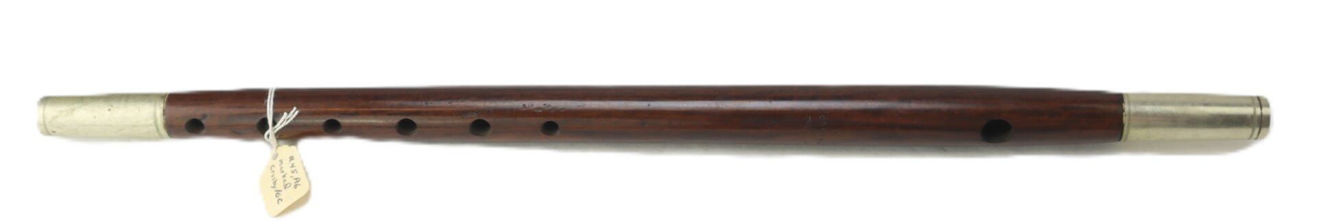 A wooden flute with six finger holes, metal fittings at both ends, and a small tag tied near one end.
