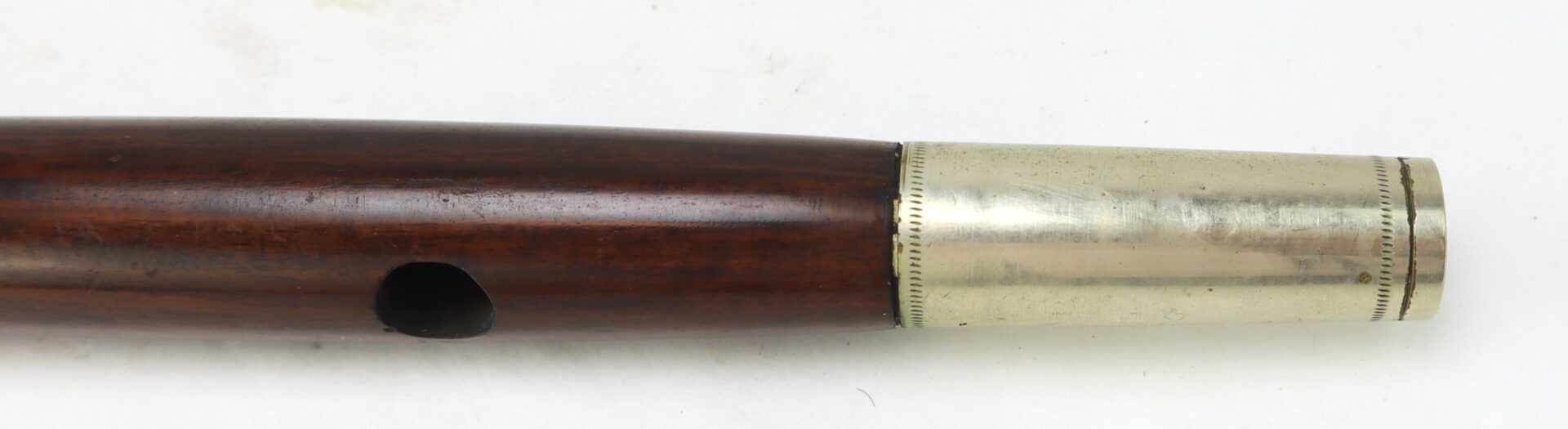 A close-up of a wooden wind instrument with a metal end and a single finger hole visible against a white background.