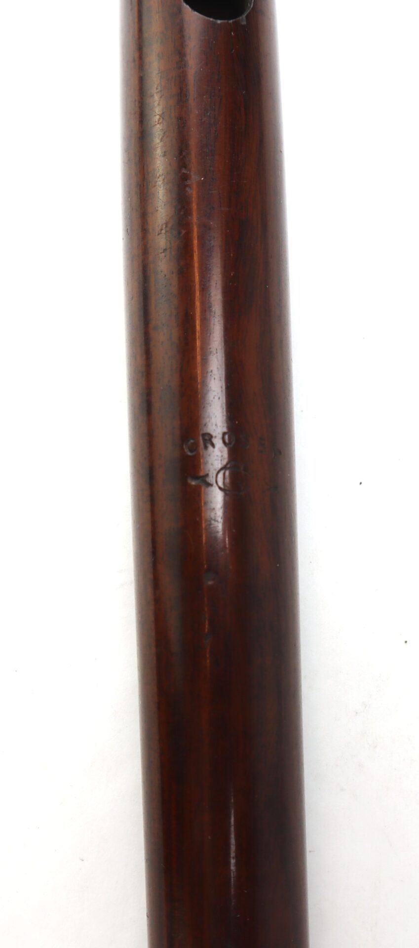 Close-up of a polished wooden object with visible grain and a stamped mark that reads "CROSS" along with an unclear symbol or logo beneath it.