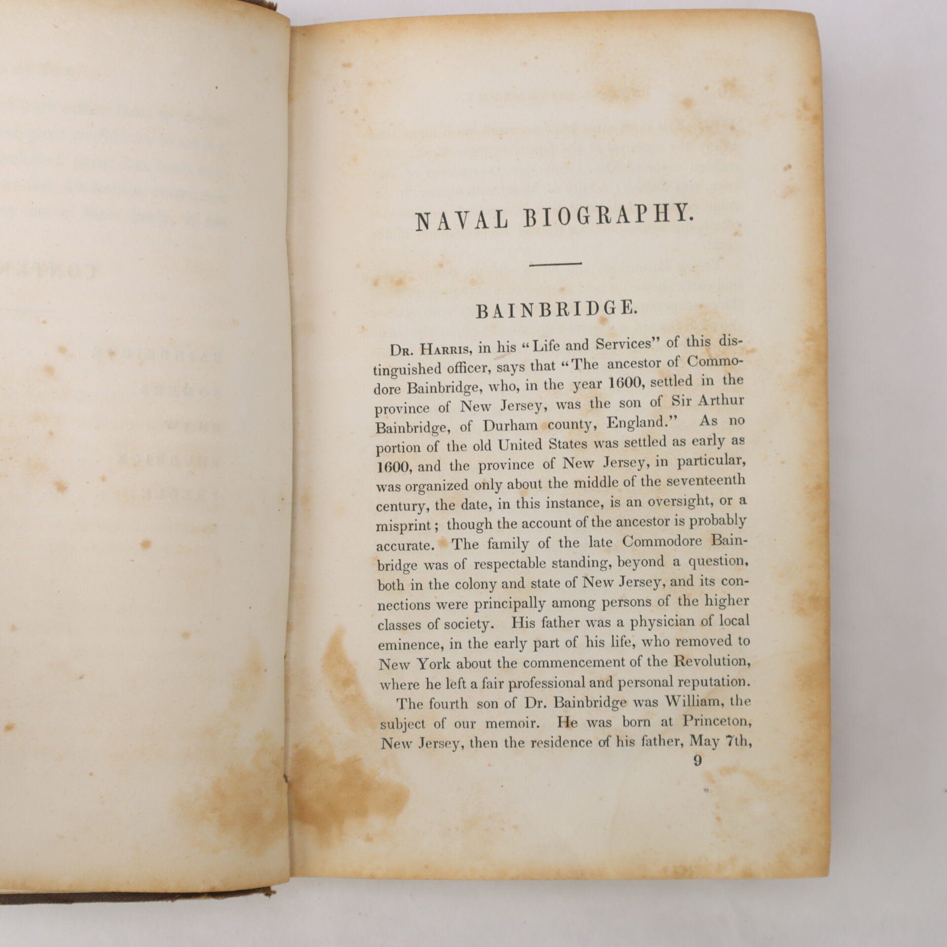 An open book displays a page titled "Naval Biography. Bainbridge," detailing the ancestry and early life of Commodore Bainbridge, with text printed in black on cream-colored paper.
