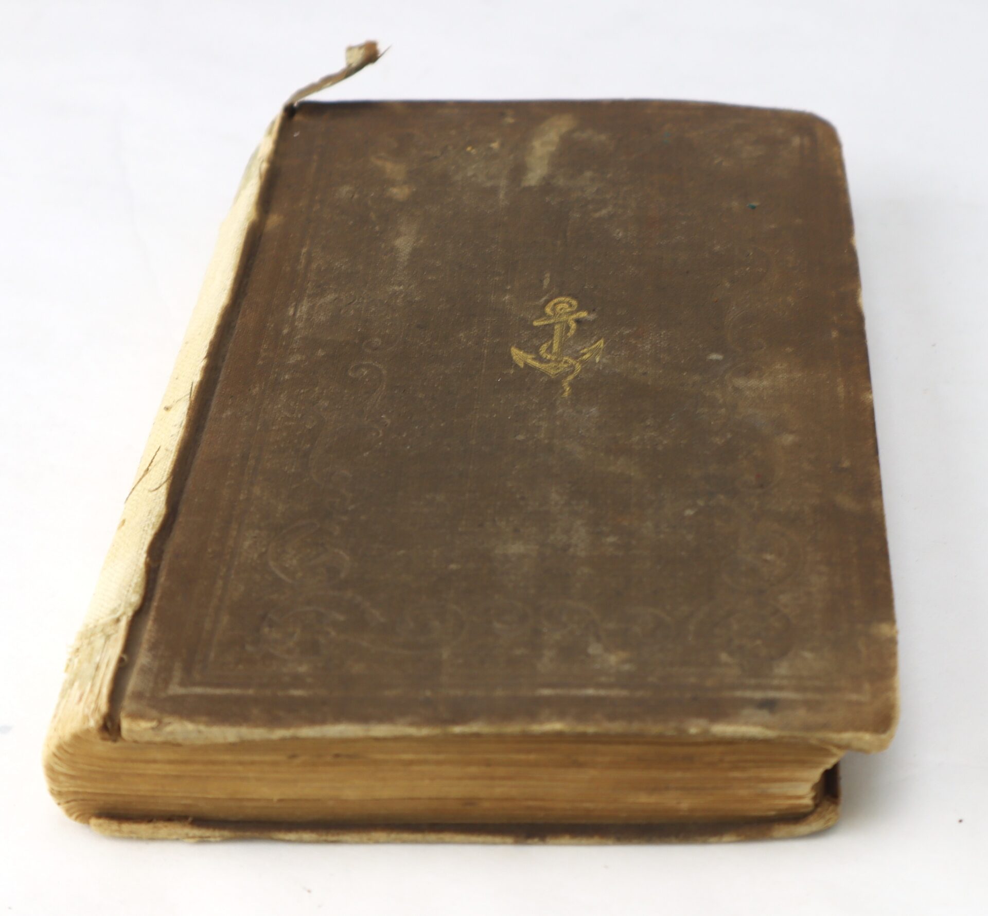 Worn, brown hardcover book with visible spine damage and a small anchor emblem on the front cover, placed on a white surface.