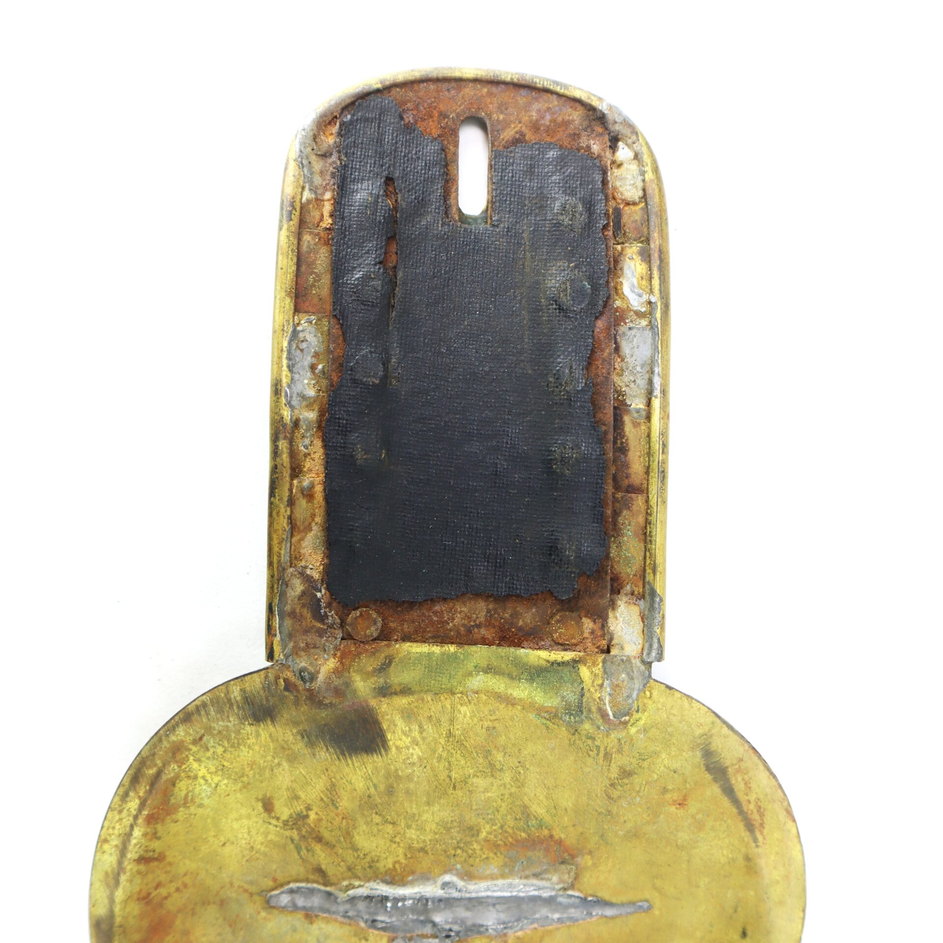 A close-up view of a worn, partially rusted brass object with a rectangular black section in the center and visible corrosion along the edges.