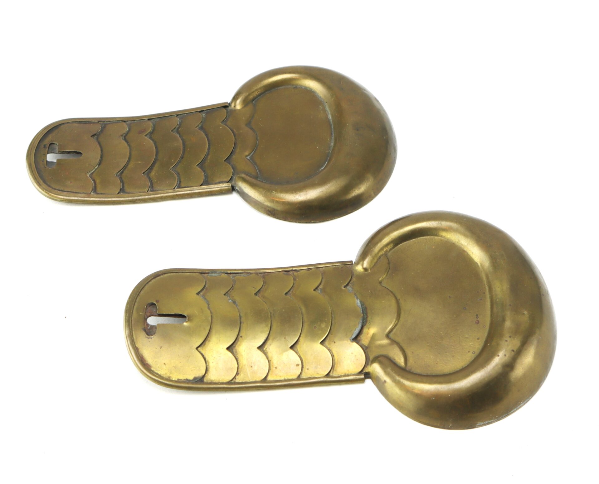 Two brass objects with rounded ends and scale-like engravings, each with a slot near one end, displayed on a white background.
