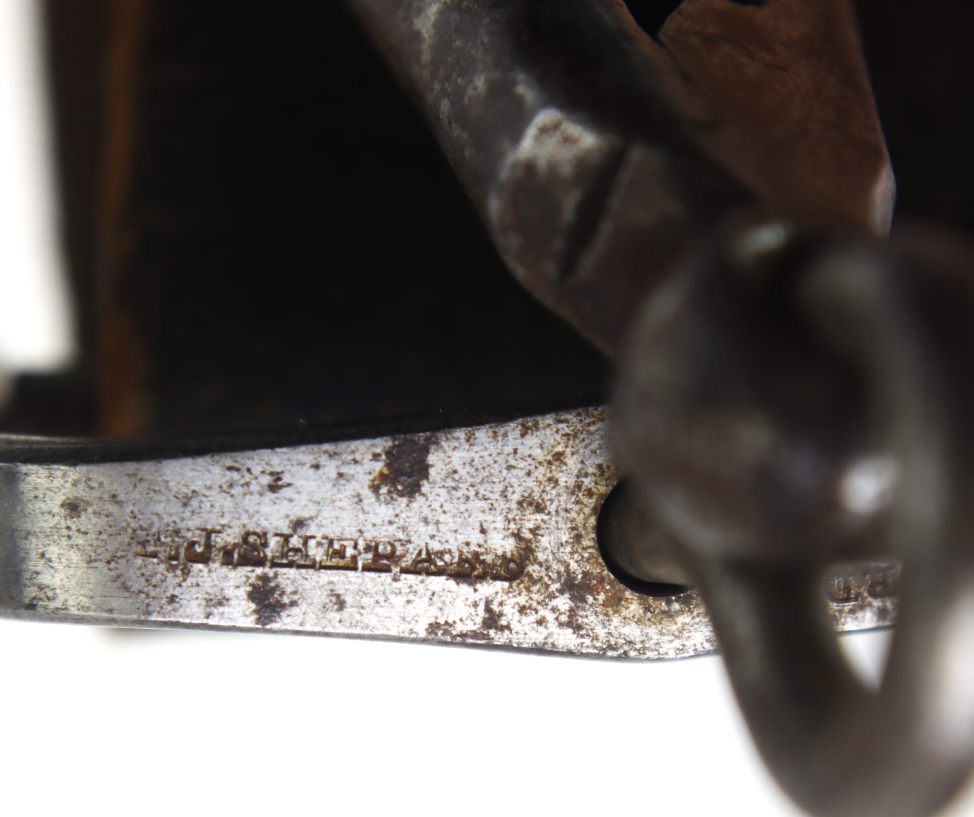 Close-up of a weathered metal object with "P.J. SLEEPAR" engraved on its surface and a metal chain attached.