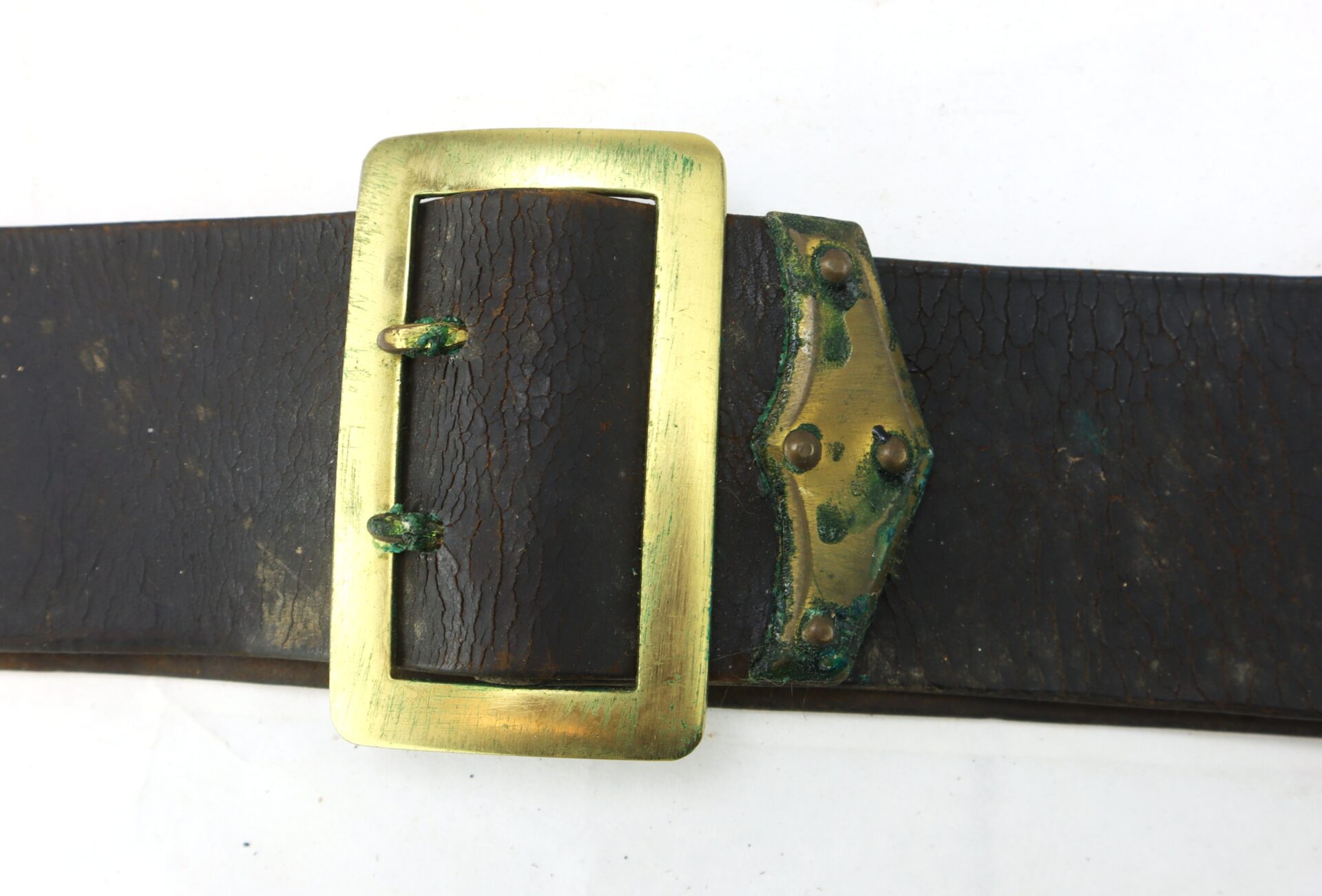 A close-up of the Cavalry Carbine Sling, featuring a worn dark leather strap and a large rectangular brass buckle with tarnish and corrosion.