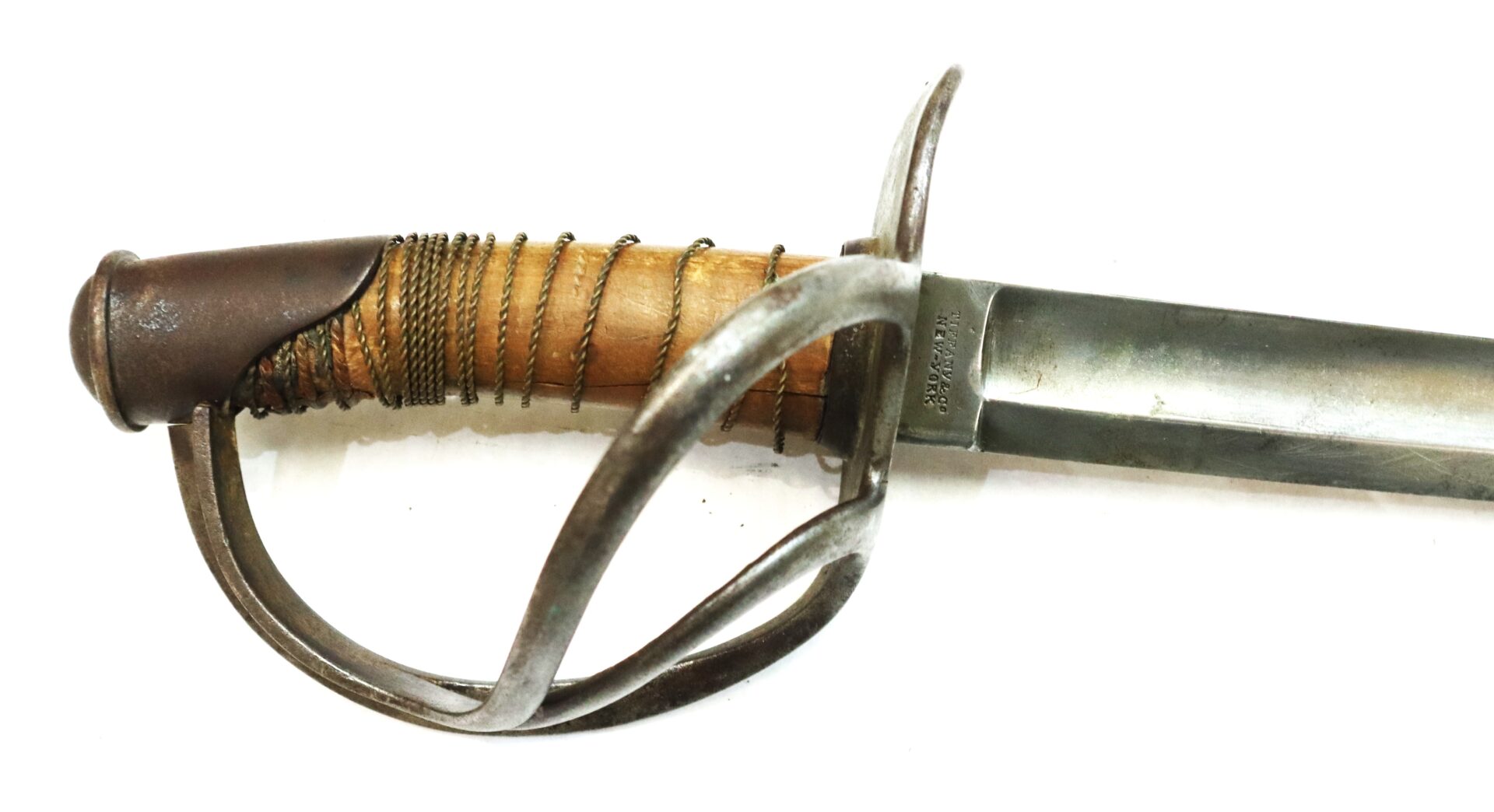 Close-up of an antique sword with a wooden grip wrapped in wire and a metal guard, blade partially visible on a white background.