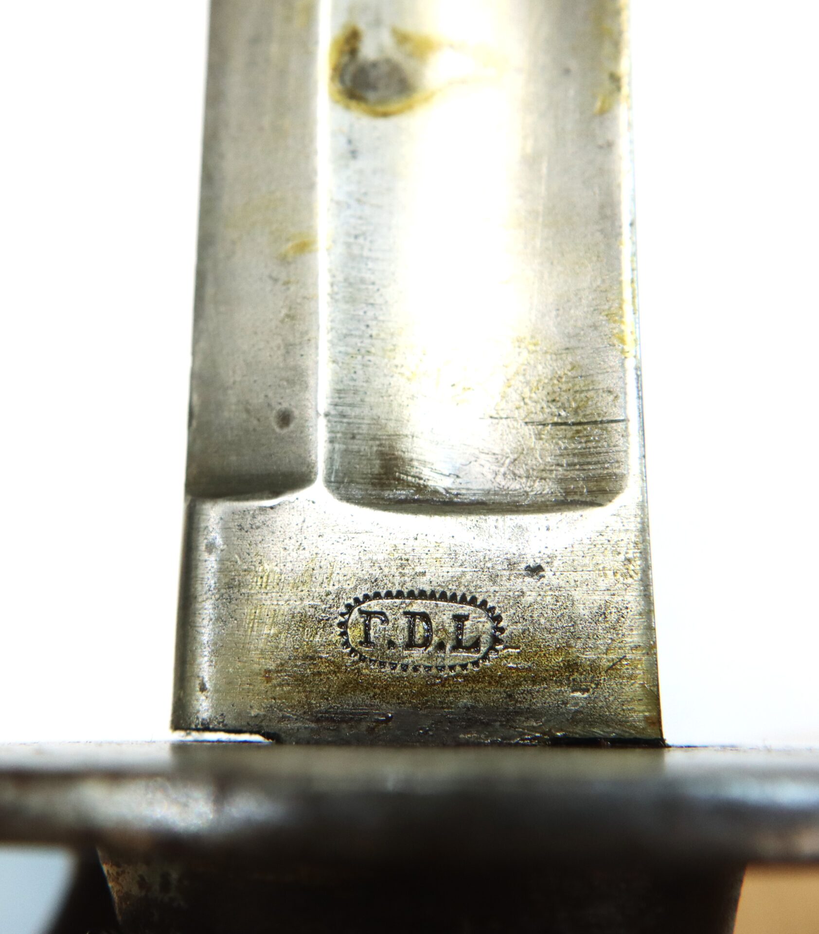 Close-up of a metal blade with the engraved initials "T.D.L" inside an oval dotted border near the base.