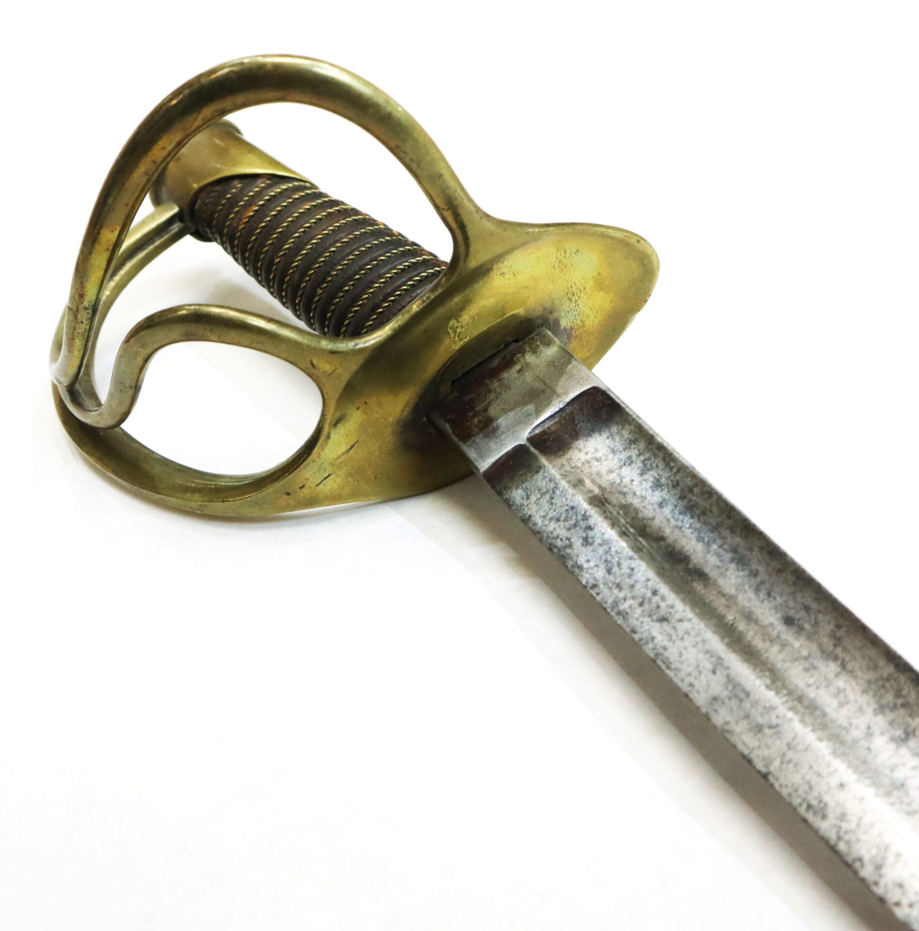 Close-up of an antique sword with a brass handguard and a slightly tarnished, straight metal blade on a white background.
