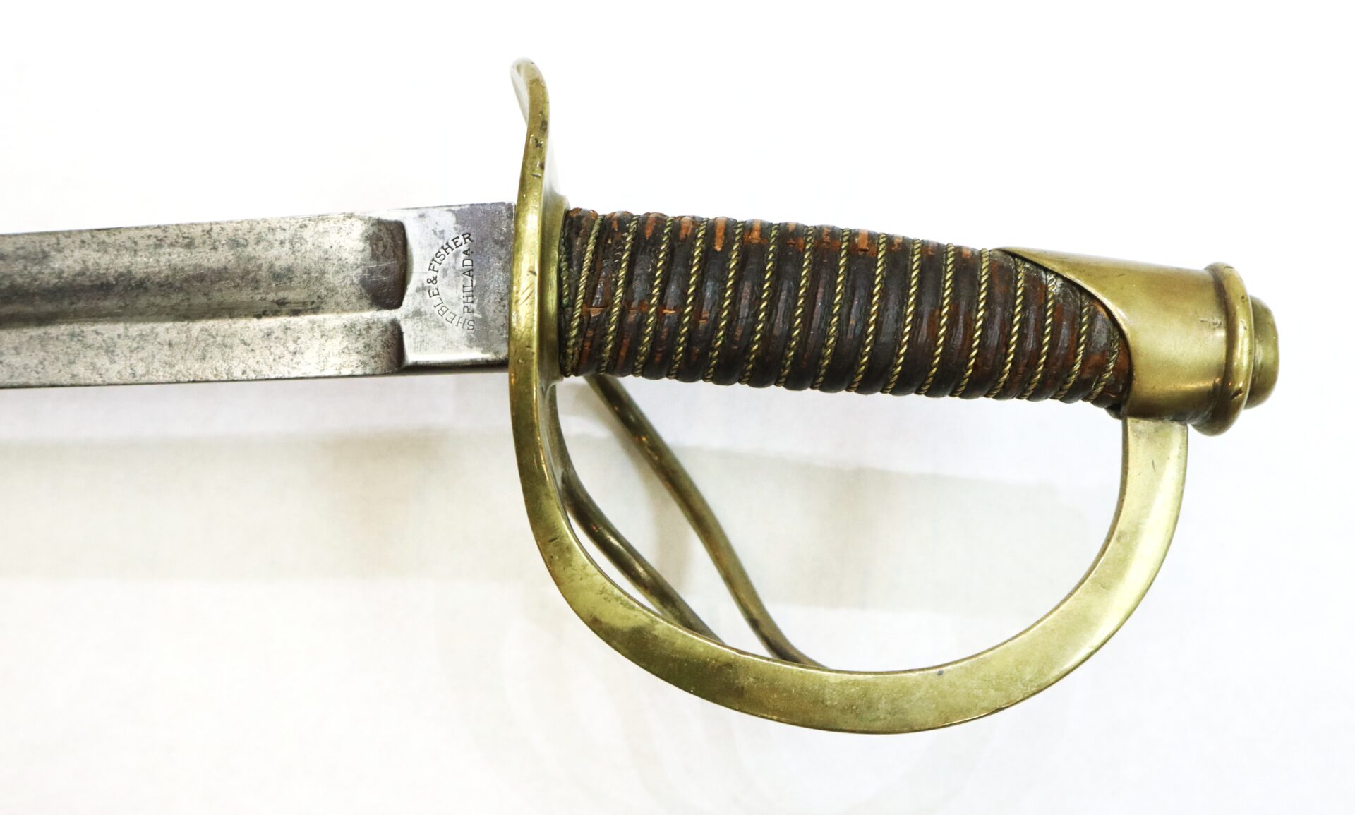 Close-up of an antique sword hilt with a brass guard and wrapped grip, showing part of the blade and faint maker's mark.
