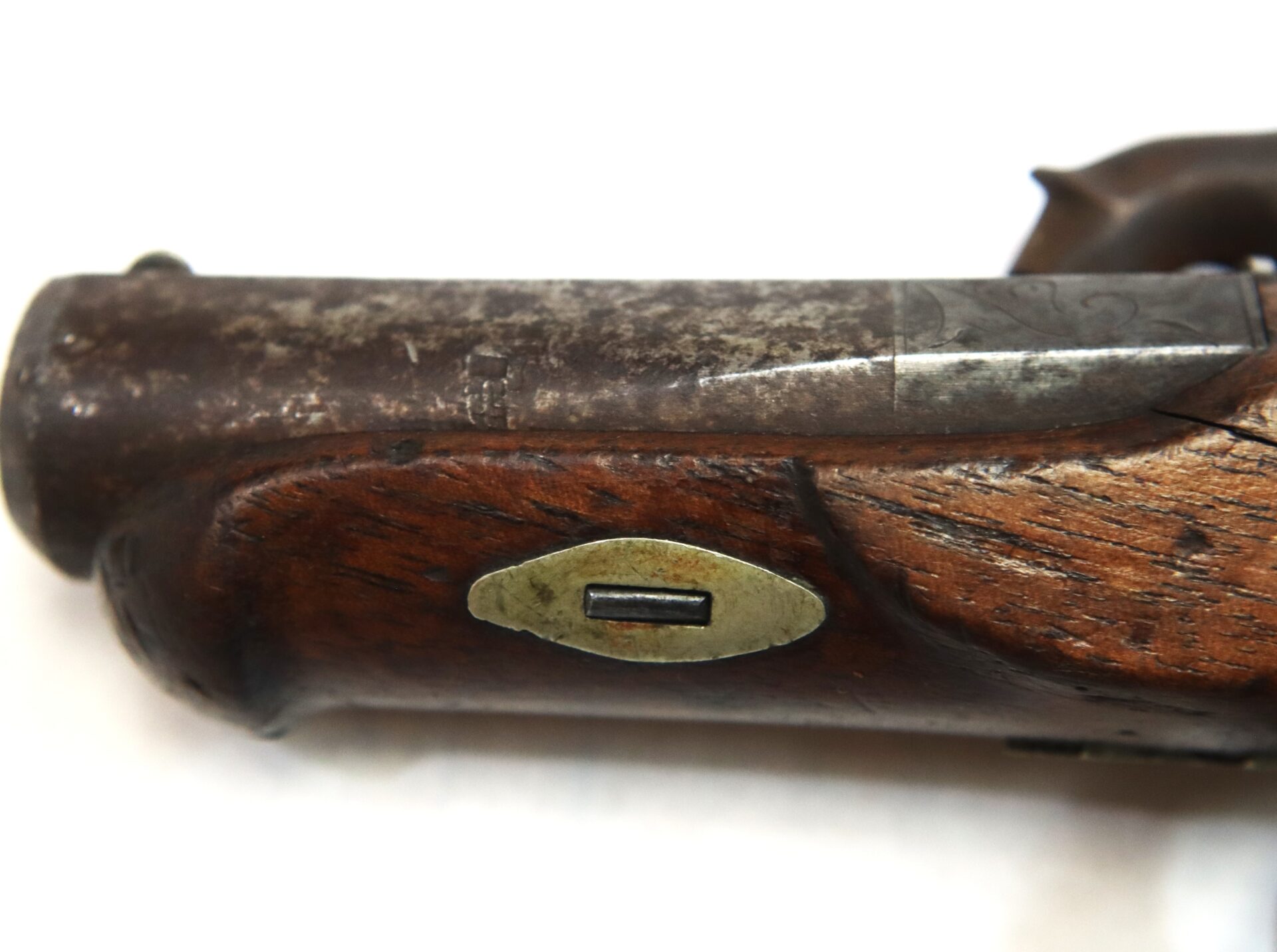 Close-up of a worn, antique wooden firearm stock with a metal plate embedded in the wood, showing signs of age and use.