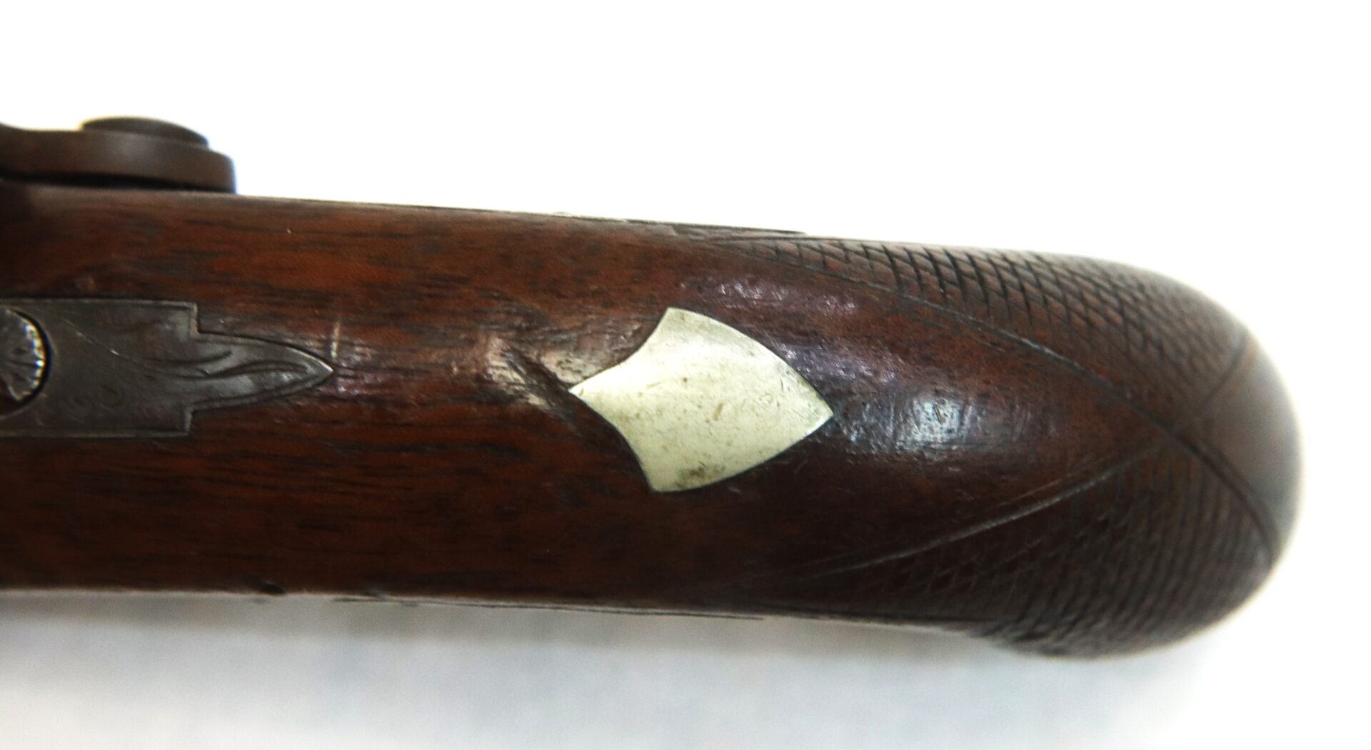 Close-up of a wooden gun handle with a diamond-shaped inlay and fine engraved patterns along the grip.