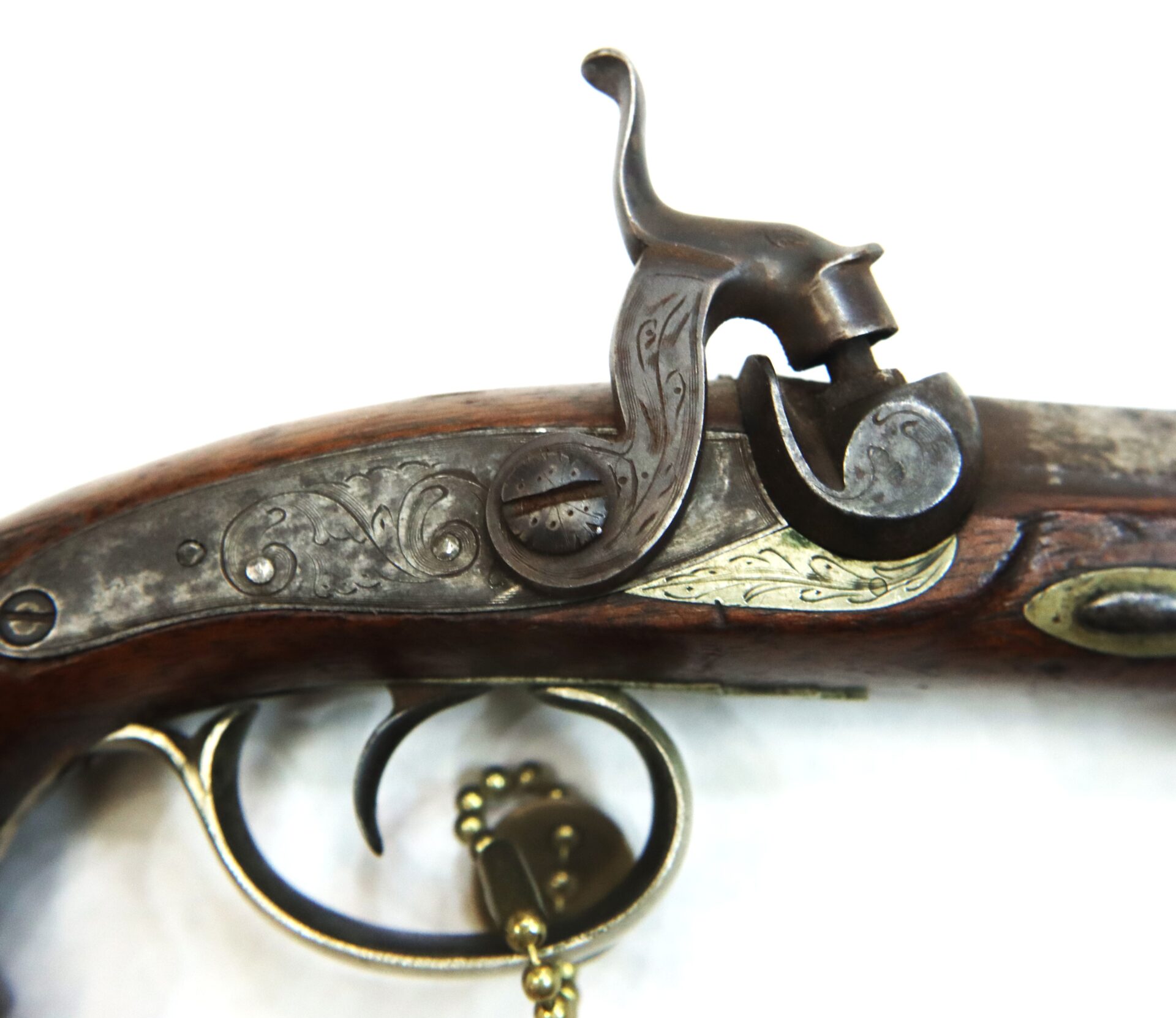 Close-up of an antique flintlock pistol showing the trigger, hammer, and engraved metal detailing on the wooden handle.