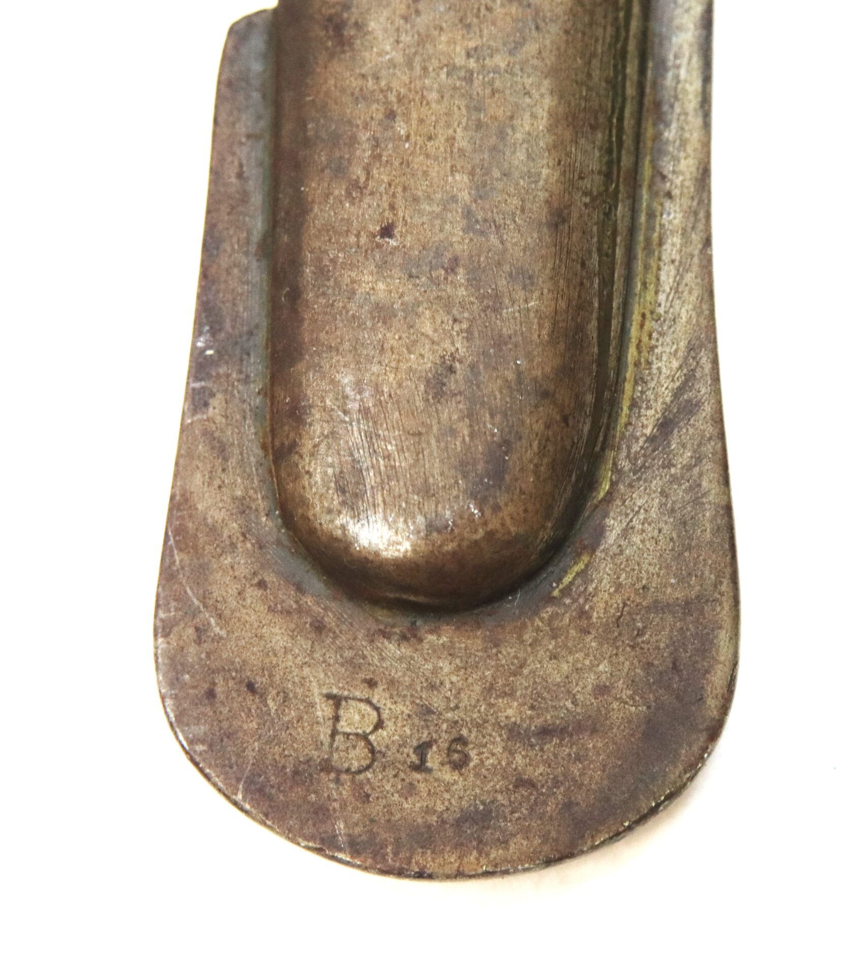 Close-up of a worn, metallic object with a rounded end, engraved with the letter "B" and the number "16" near the edge.